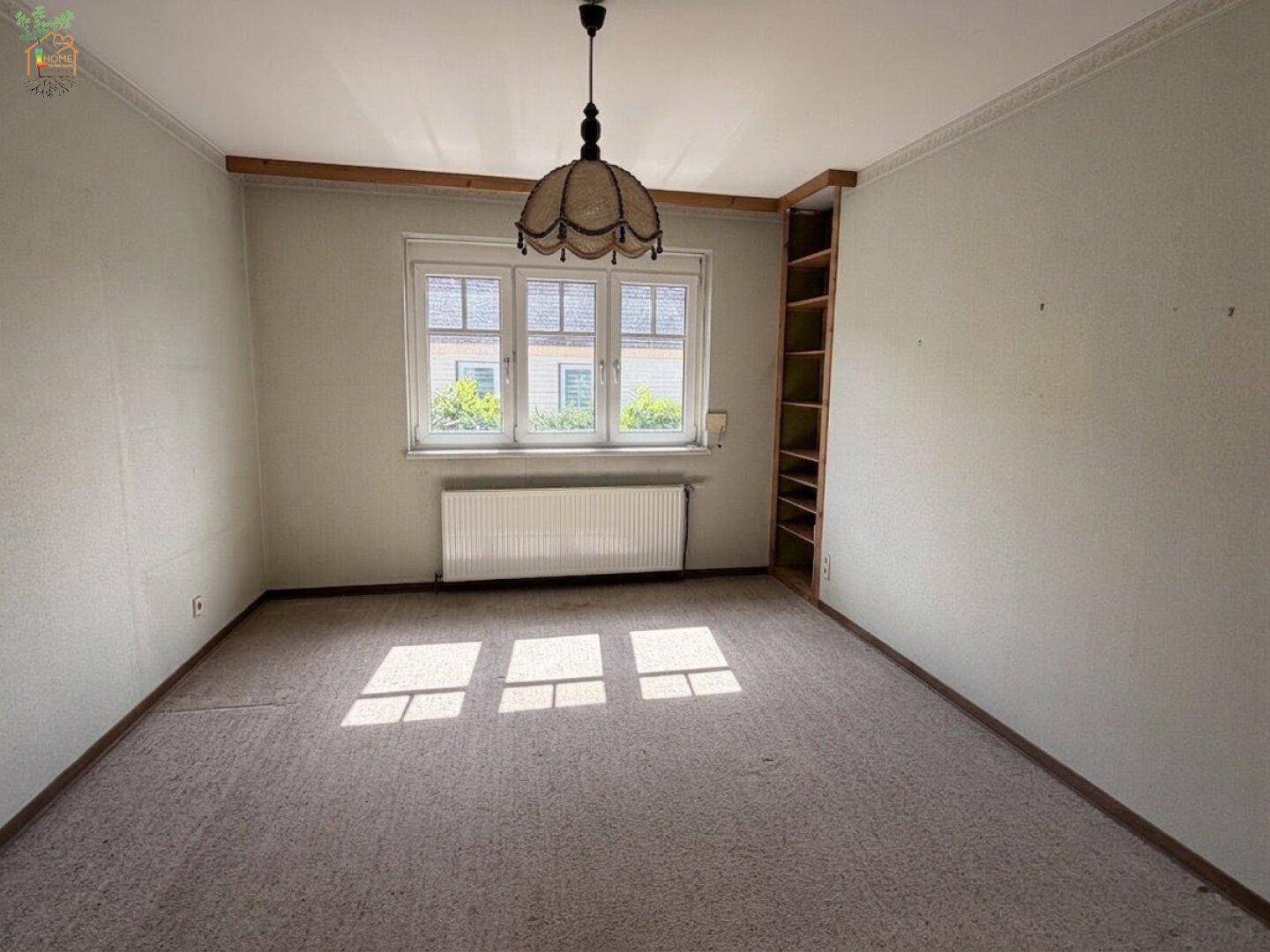 Helles Wohnzimmer mit Teppichboden, Einbauregal und Blick ins Grüne.