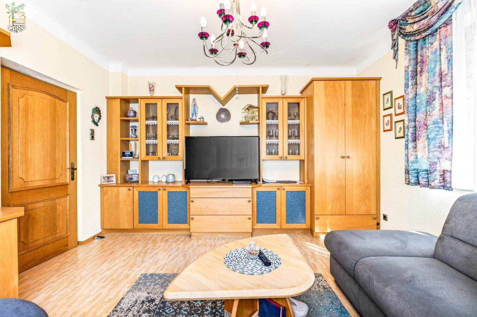 Gemütliches Wohnzimmer mit Holzmöbeln, einem großen TV-Schrank und floralen Vorhängen.