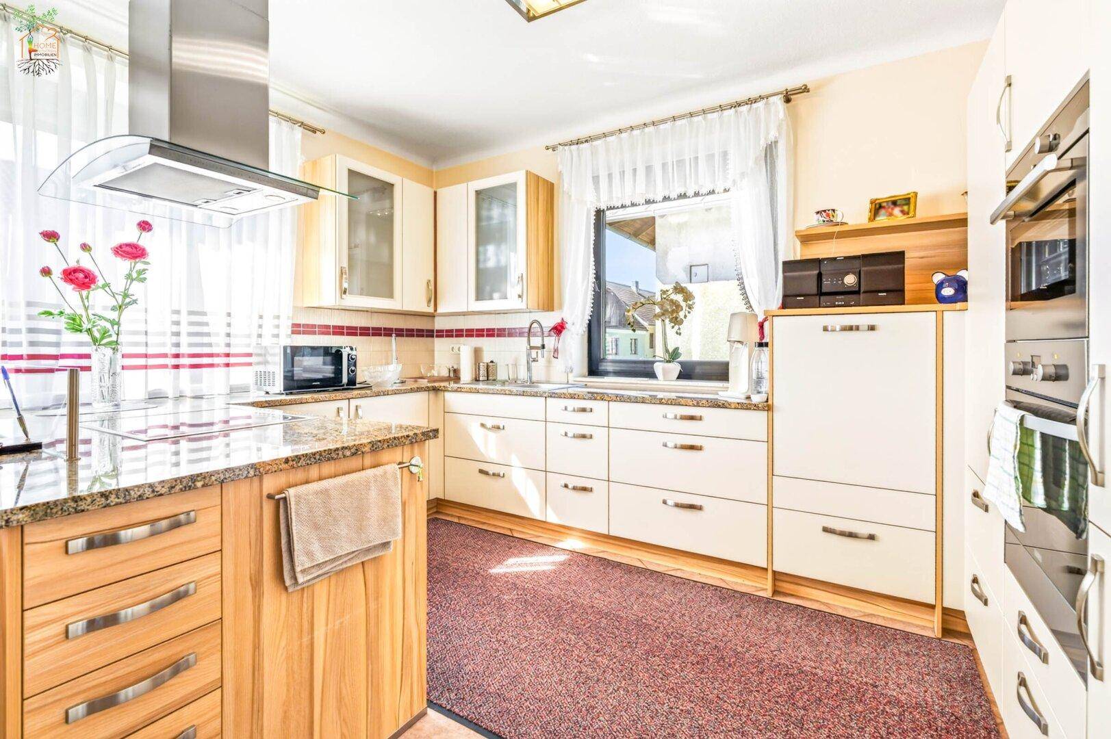Helle Küche mit beigen Fronten, Granitarbeitsplatte und modernen Einbaugeräten.