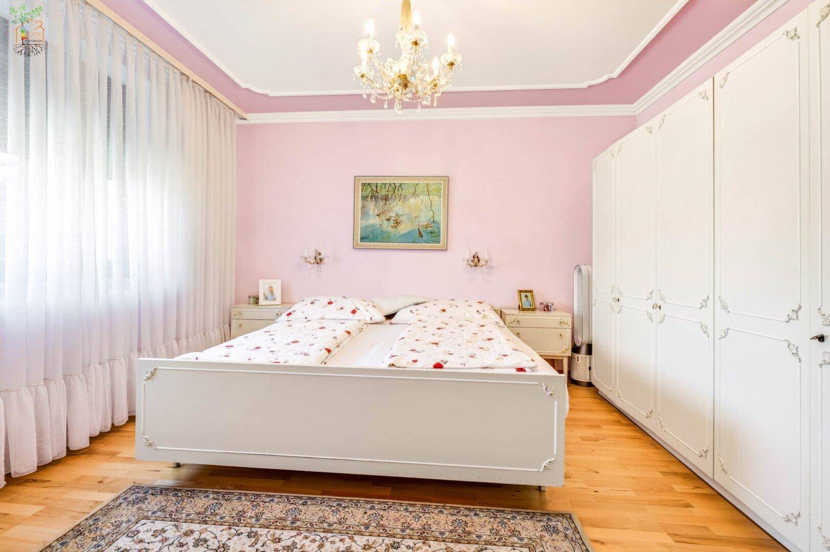 Schlafzimmer mit rosa Wänden, hellem Holzboden und einem großen weißen Kleiderschrank.