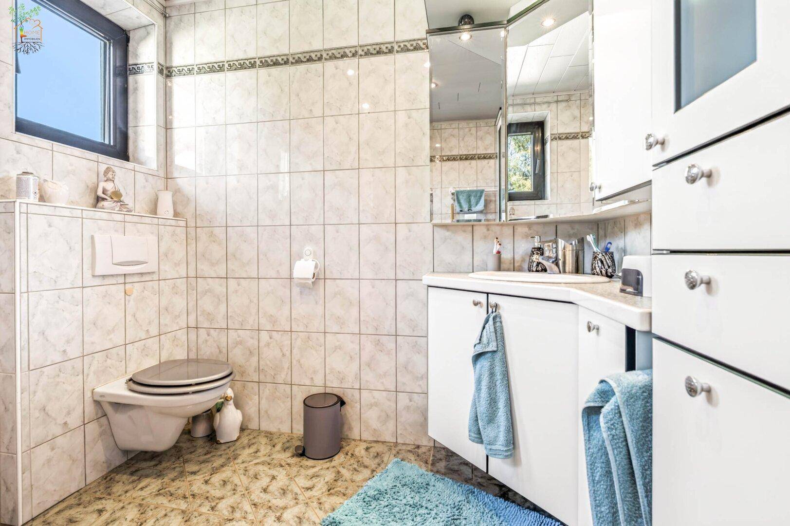 Gefliestes Badezimmer mit wandhängendem WC, Einzelwaschbecken und Spiegelschrank.