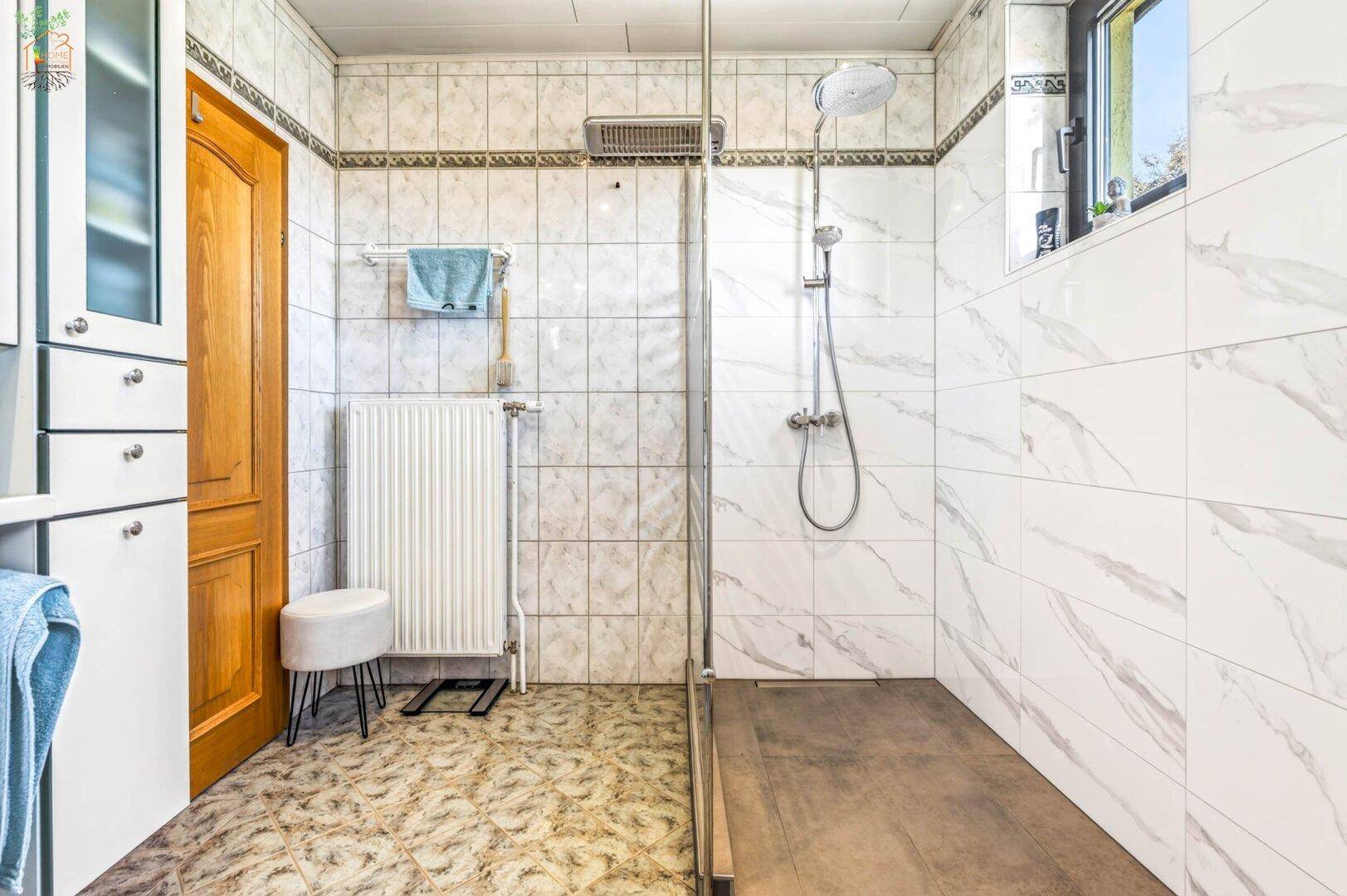 Modernisiertes Badezimmer mit ebenerdiger Dusche, Heizkörper und Fenster für Tageslicht.
