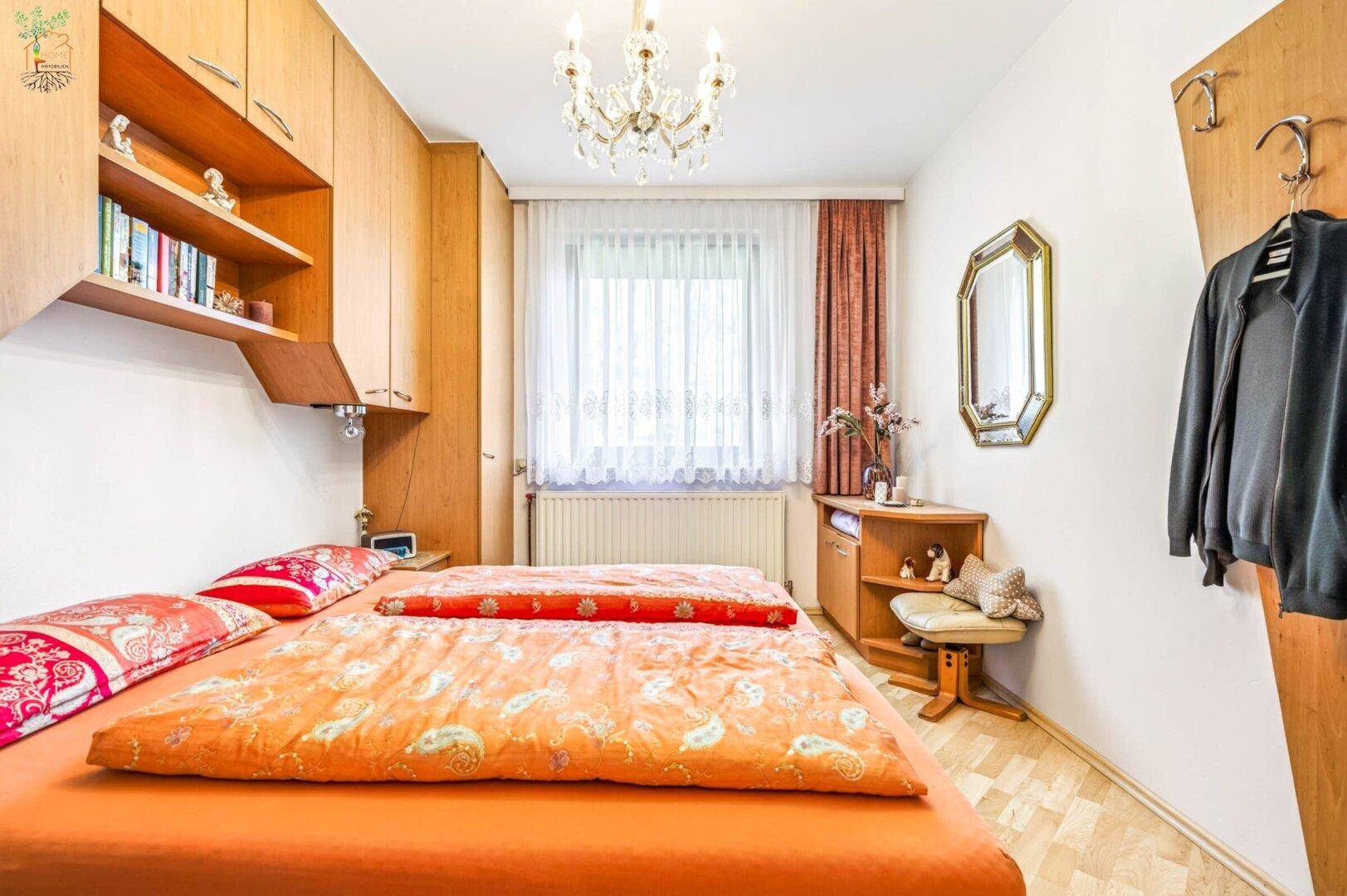 Gemütliches Schlafzimmer mit Holzmöbeln, hellem Boden und Fenster mit Vorhängen.
