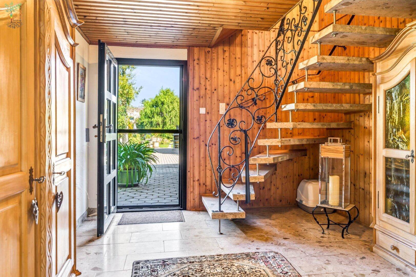 Heller Eingangsbereich mit offener Holztreppe, schmiedeeisernem Geländer und Holzwänden.