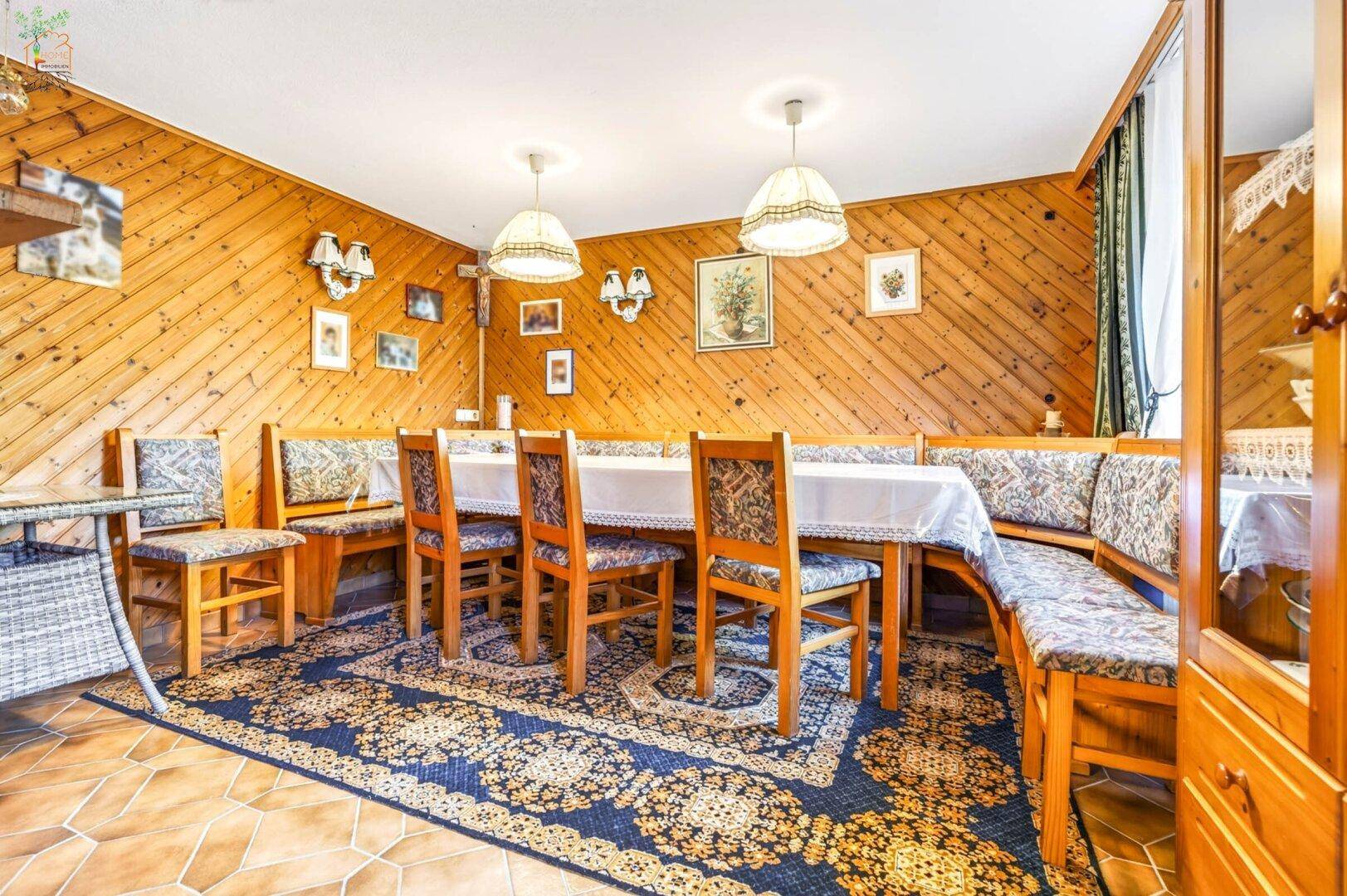 Traditioneller Essbereich mit Holzbänken, großem Esstisch und gemustertem Teppich.