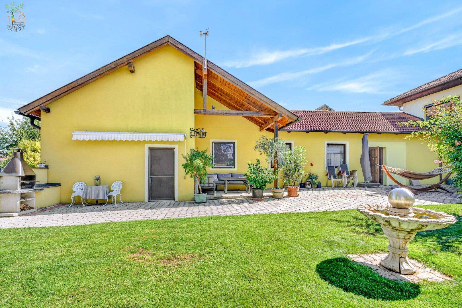 Rückansicht des Hauses mit großem Garten, Grillplatz und gepflasterter Terrasse.