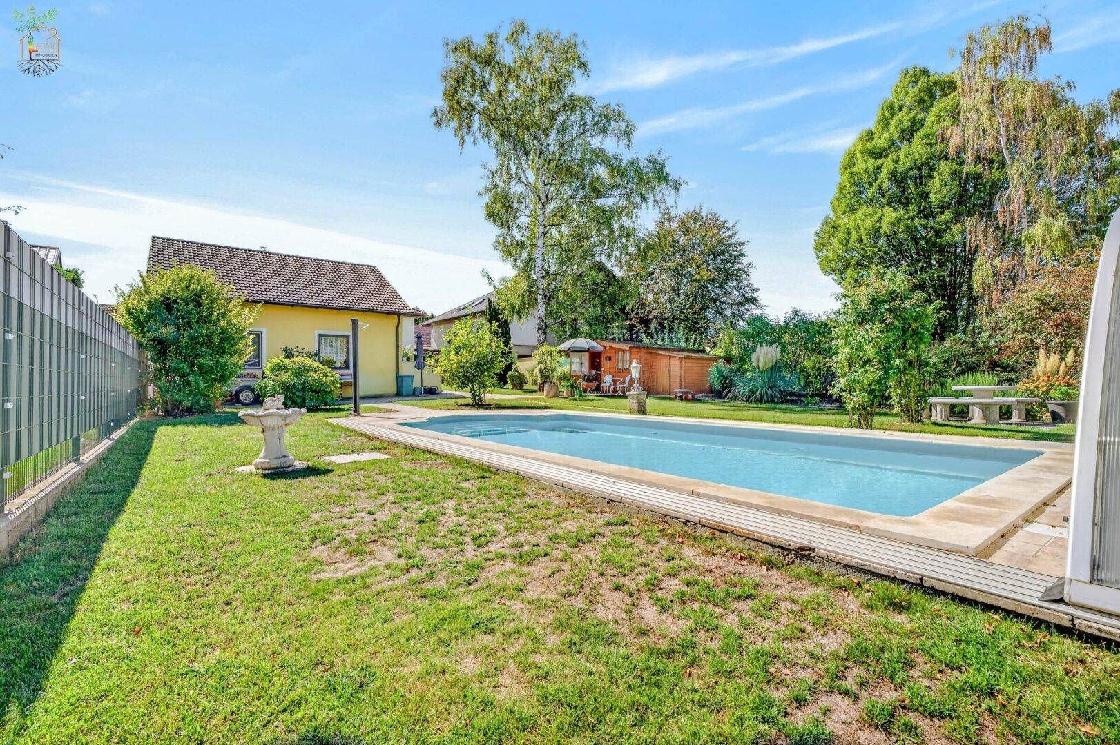 Weitläufiger Garten mit einem Swimmingpool, Rasenflächen und umgebender Bepflanzung.