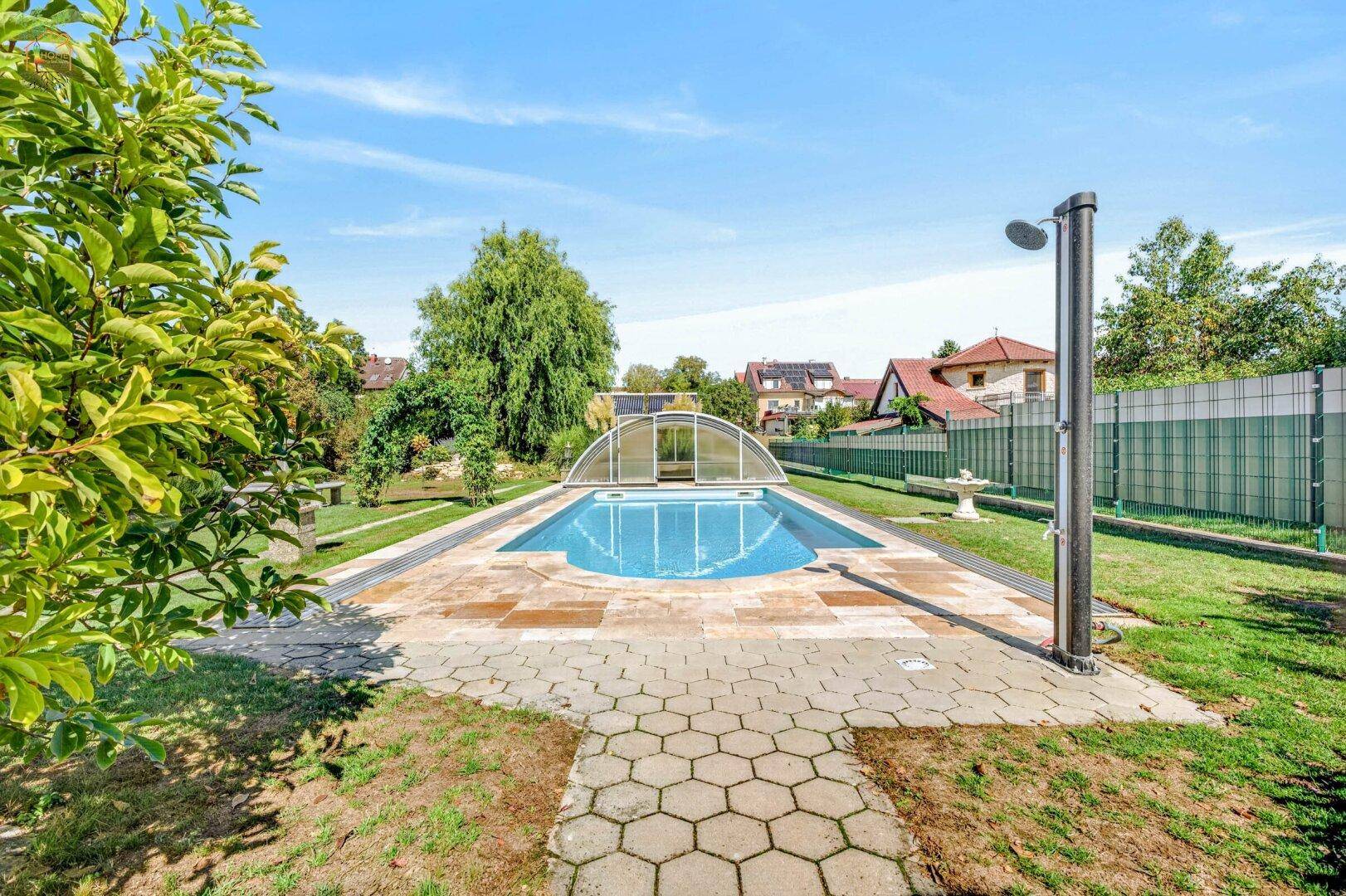 Außenbereich mit großem Swimmingpool, gepflasterter Umrandung und Außendusche.