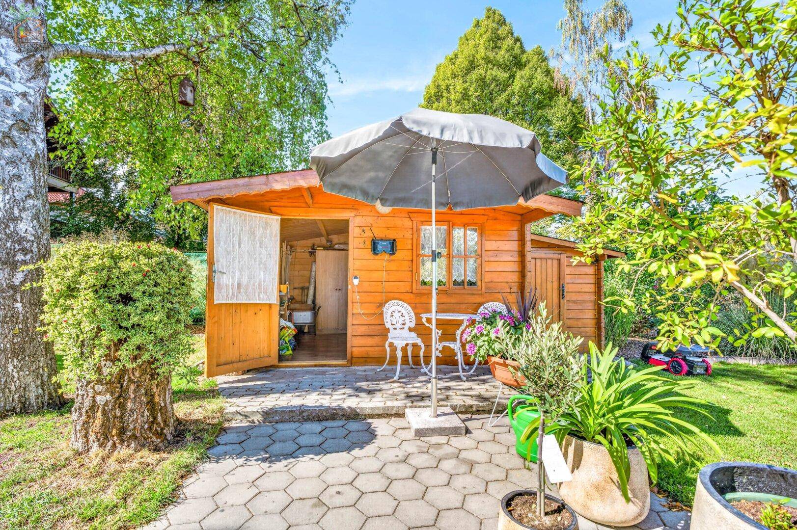 Gemütliches Gartenhaus aus Holz mit kleiner Terrasse und Sitzgelegenheiten im Grünen.