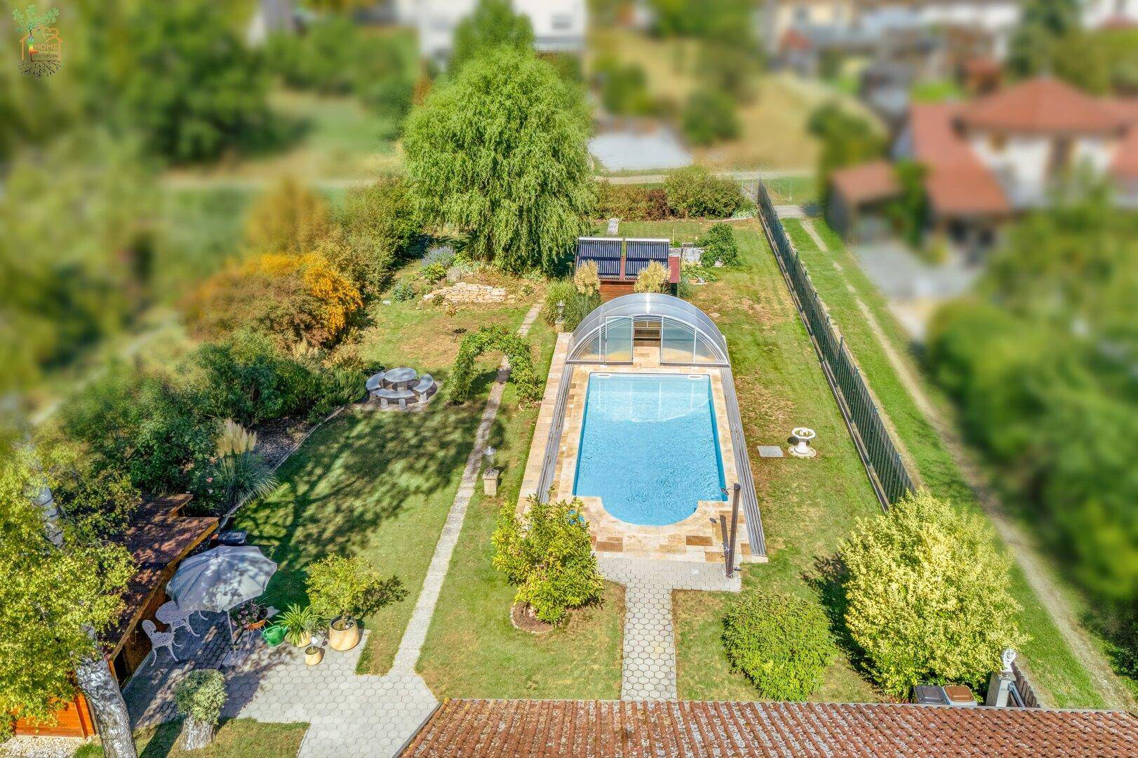 Vogelperspektive des weitläufigen Gartens mit einem überdachten Swimmingpool und gepflegten Grünflächen.