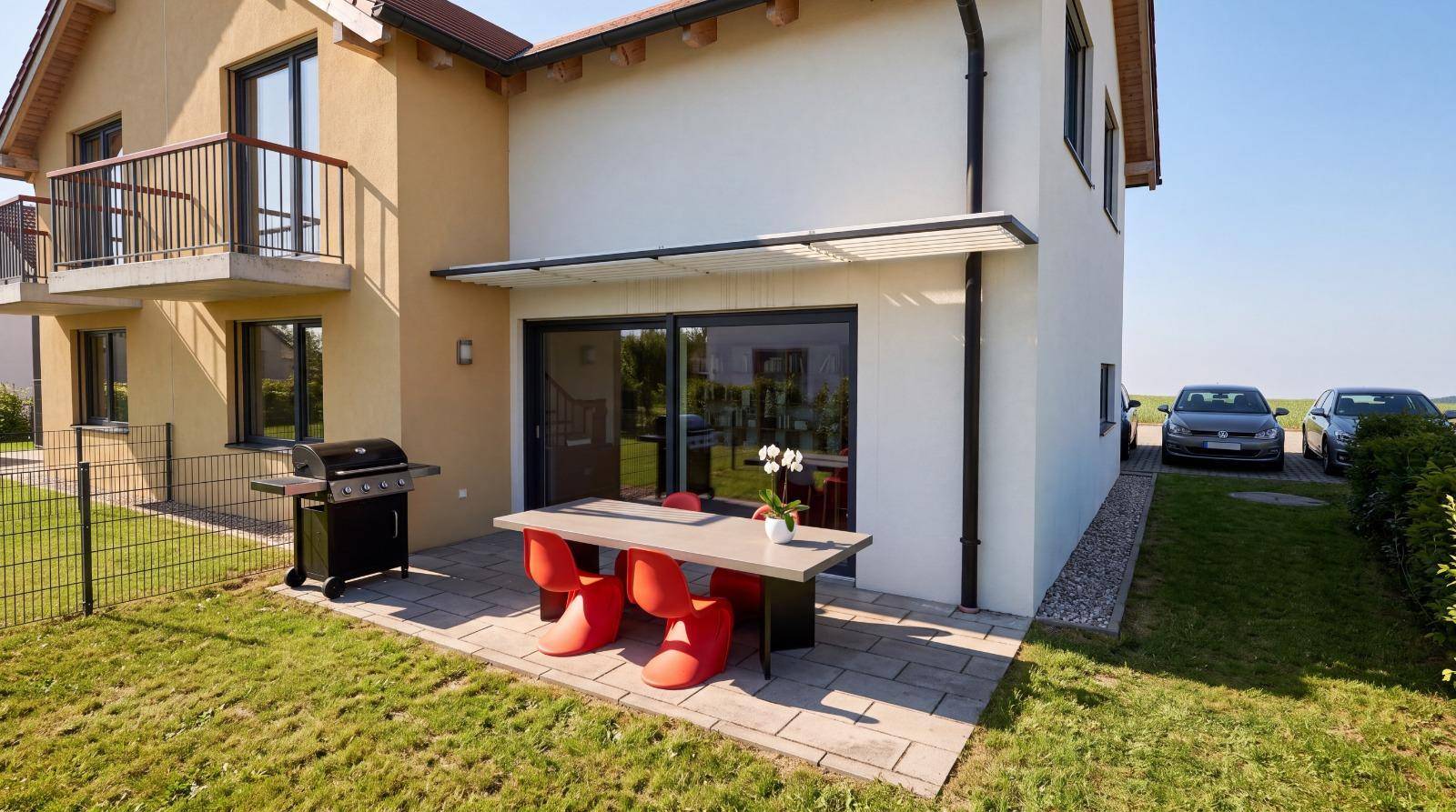 Sonnige Terrasse mit modernen Gartenmöbeln, Grill und Zugang zum grünen Garten.