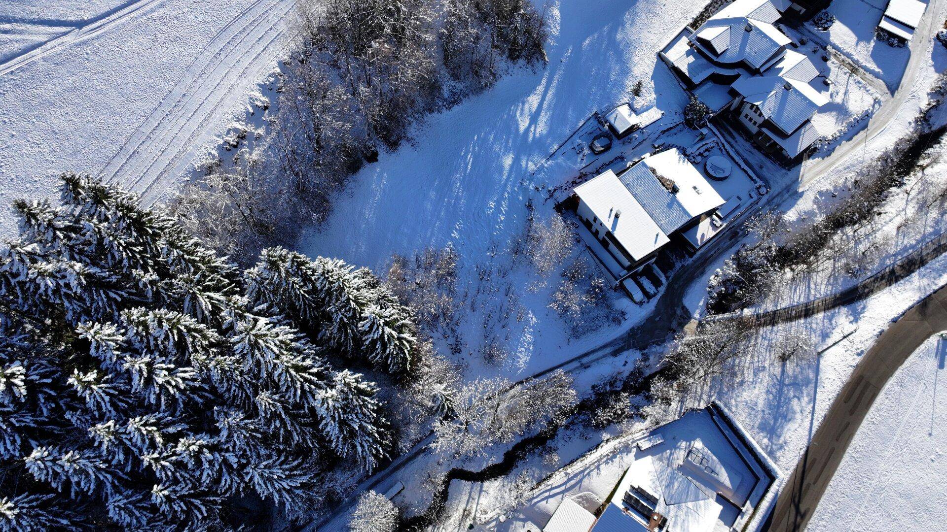 Winterliche Luftansicht einer Siedlung umgeben von verschneiten Wäldern und Feldern.