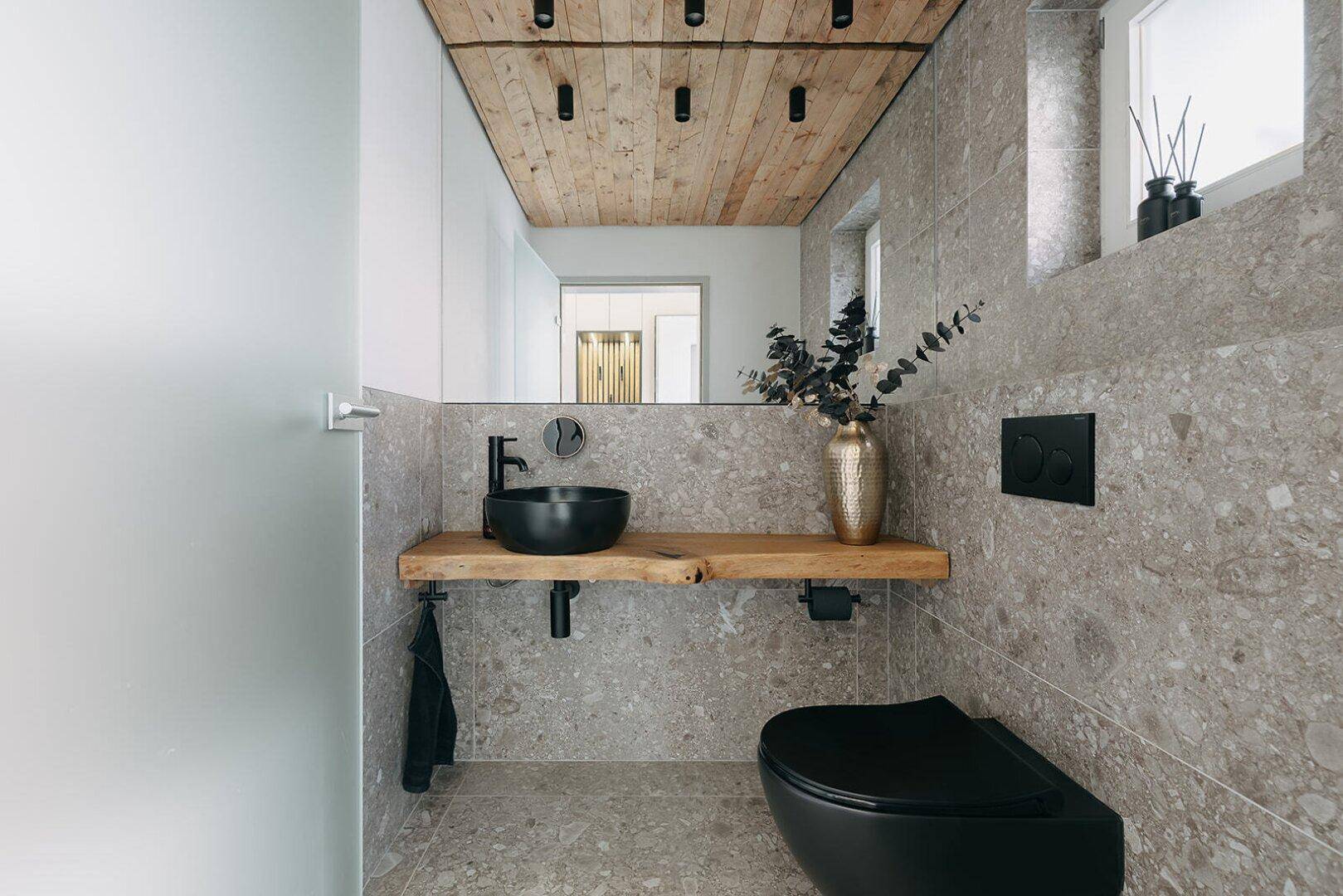 Modernes Gäste-WC mit Holzdecke, schwarzem Waschbecken und Wand-WC.
