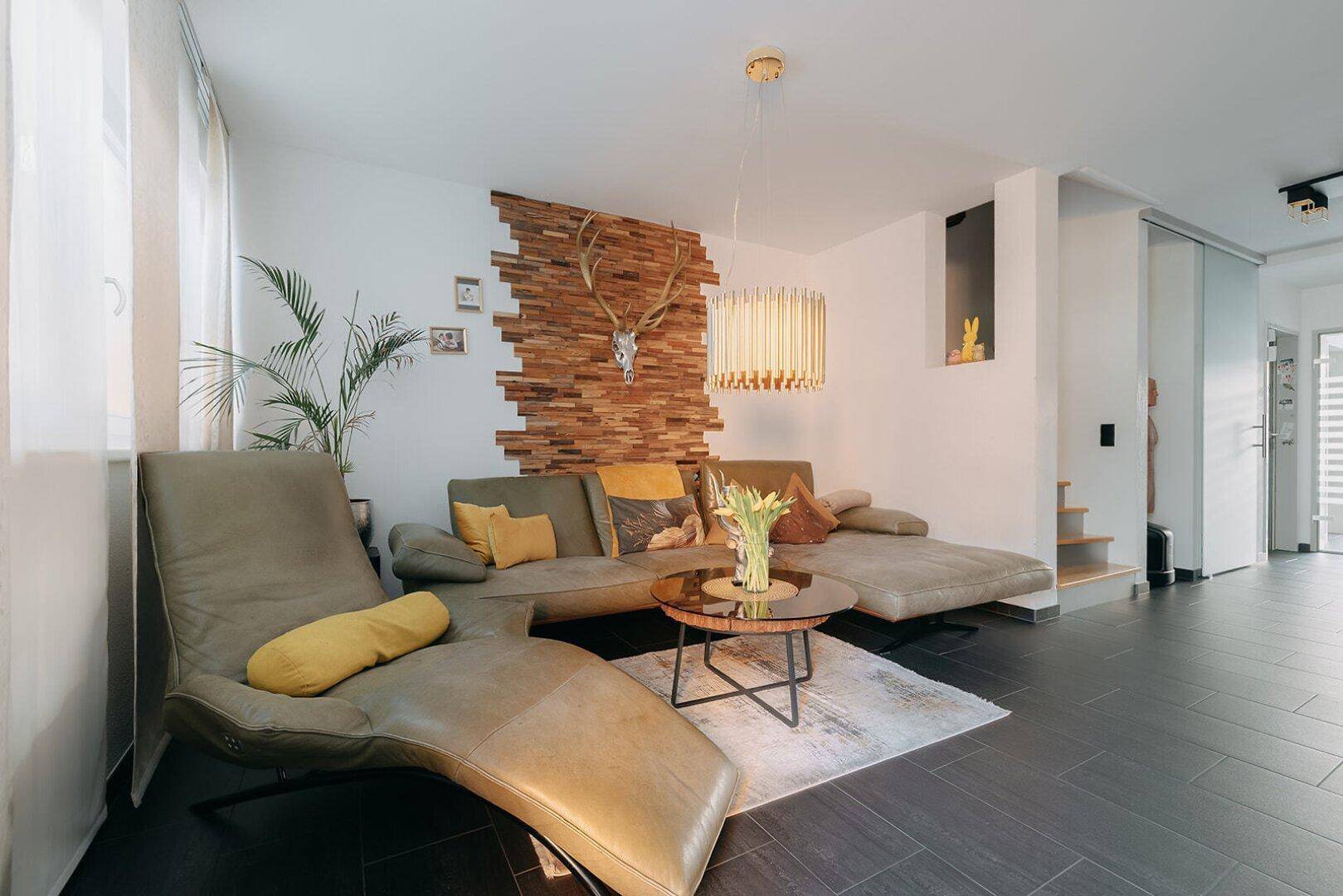Heller Wohnbereich mit bequemer Couch, Holzwanddekoration und großzügigen Fenstern.