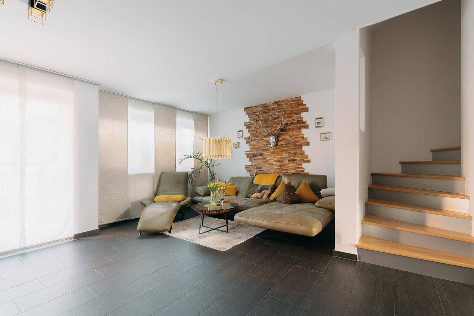 Geräumiges Wohnzimmer mit dunklen Fliesen, bequemer Couch und dekorativer Holzwand.