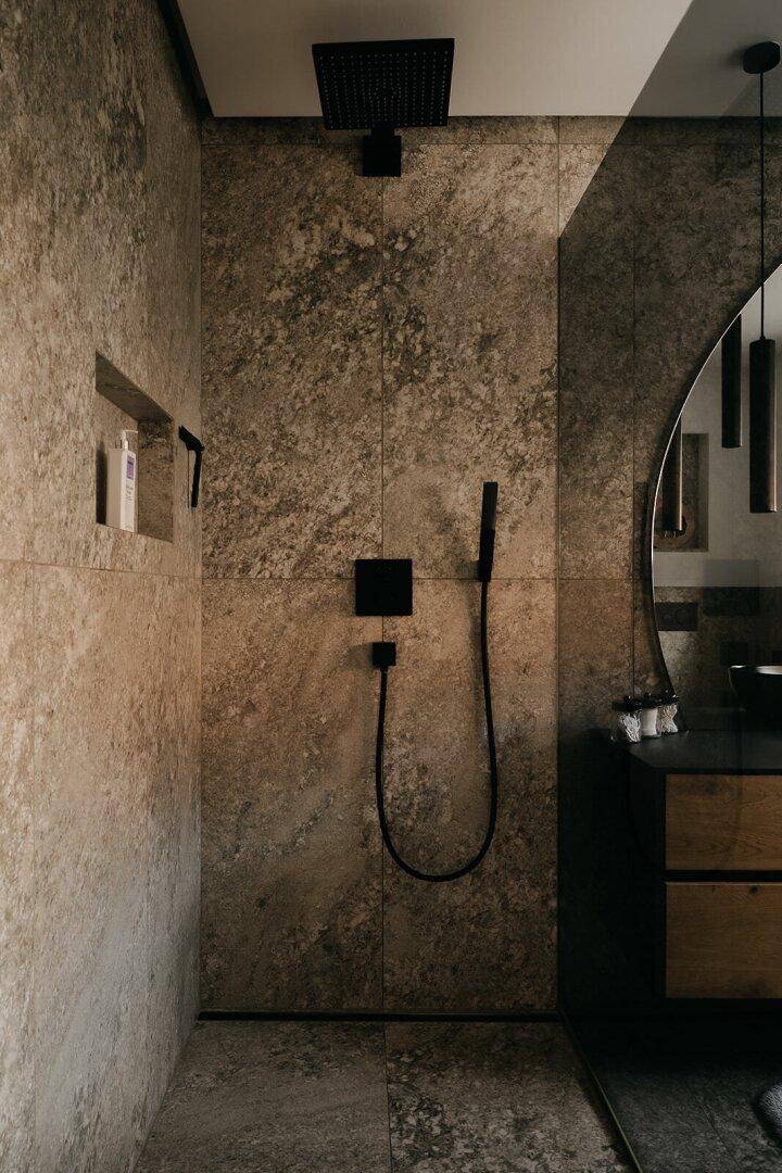 Detailansicht der begehbaren Dusche mit schwarzer Regendusche und Natursteinfliesen.