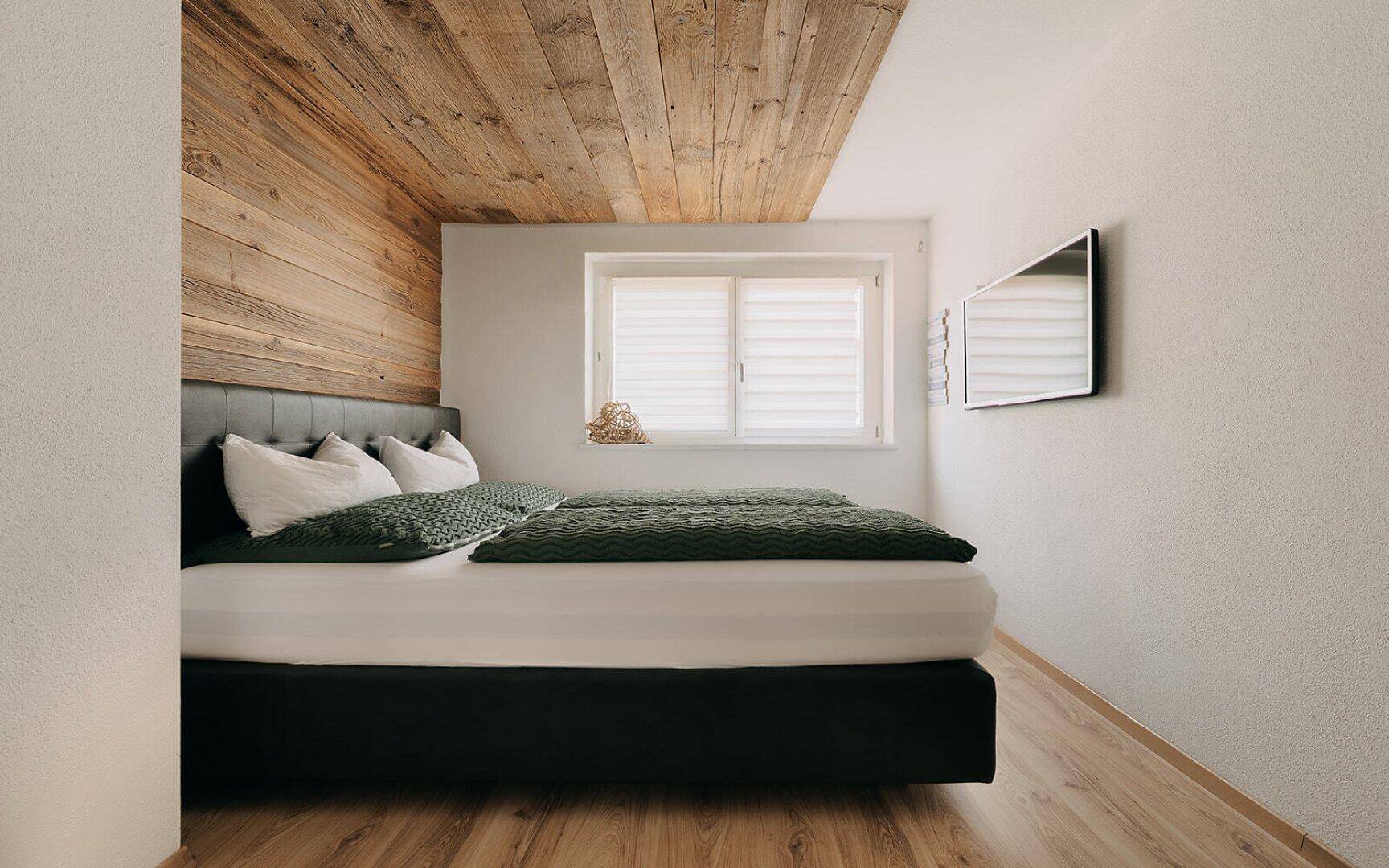 Gemütliches Schlafzimmer mit Holzboden, Holzwand und Dachschräge.