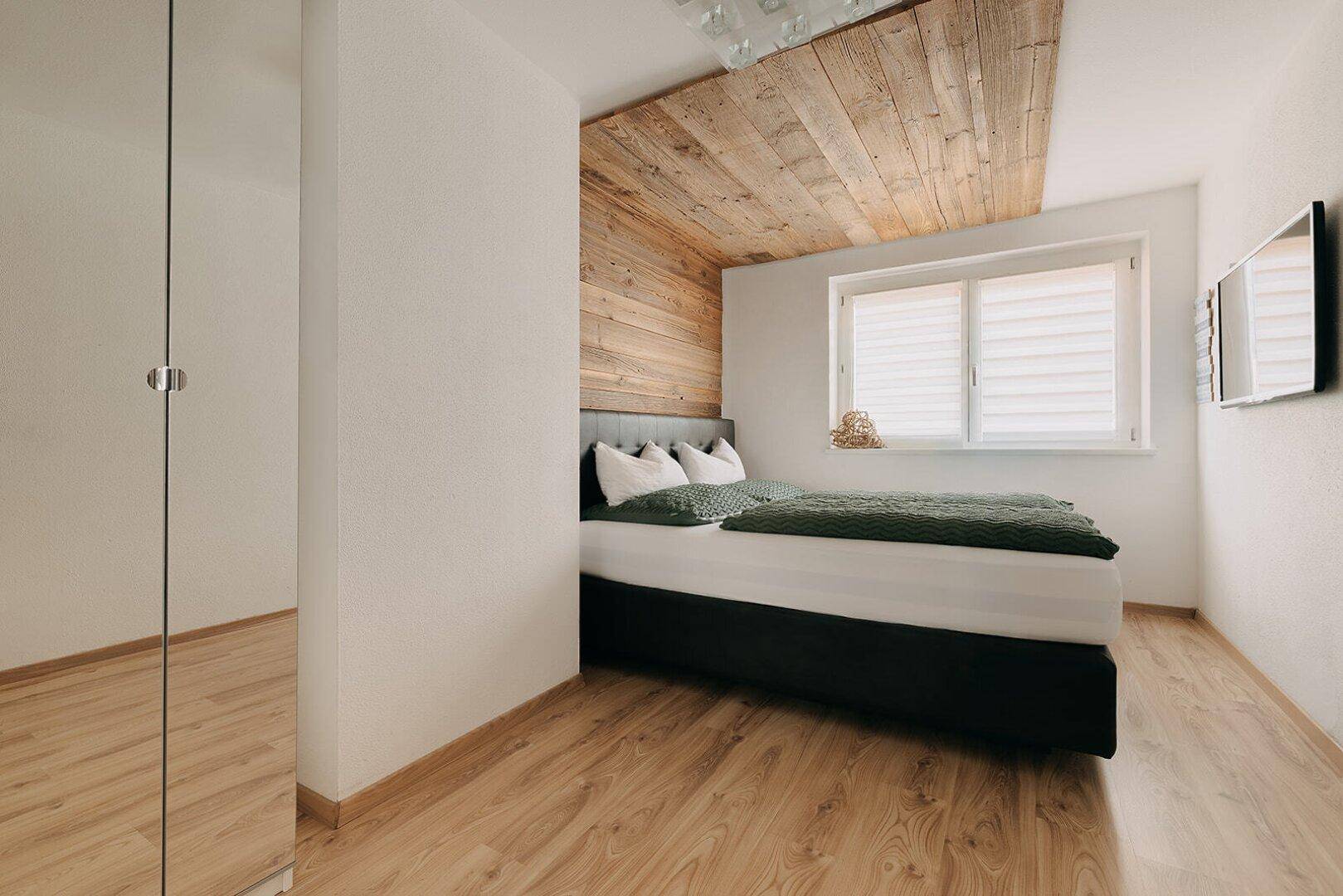 Helles Schlafzimmer mit Holzboden, Holzwand und Dachschräge, inklusive Spiegelschrank.