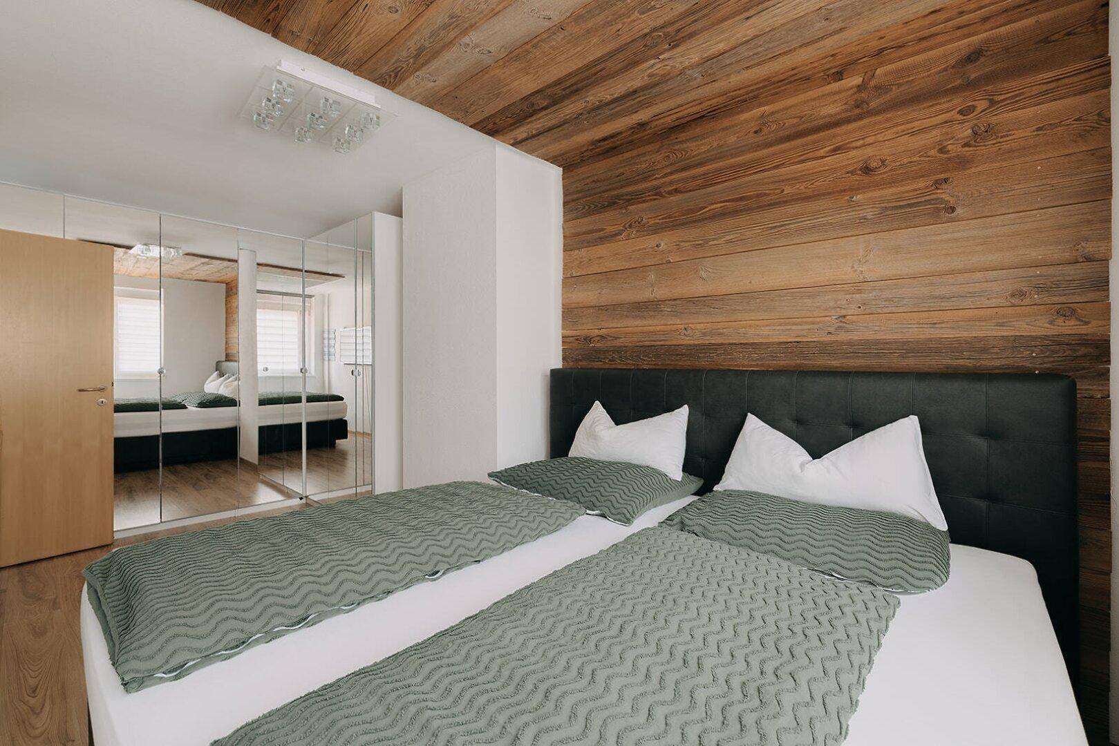 Schlafzimmer mit Holzboden, Holzwand und Spiegelschränken, die den Raum optisch vergrößern.