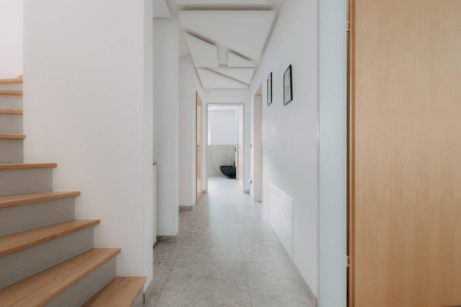 Heller Flur mit Holztreppe und modernen Fliesen, der verschiedene Bereiche verbindet.