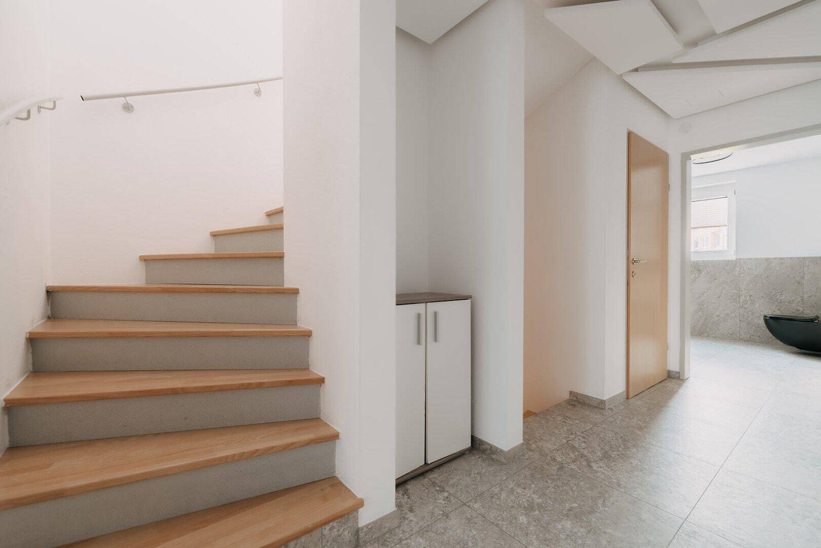 Heller Flur mit Holztreppe und modernem Design, der zu den oberen Etagen führt.
