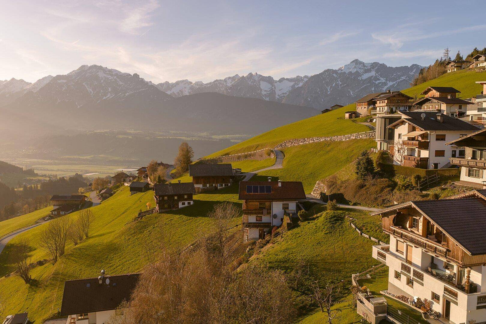 Häuser auf einem grünen Hang mit weitem Blick auf die majestätischen Berge unter einem klaren Himmel.
