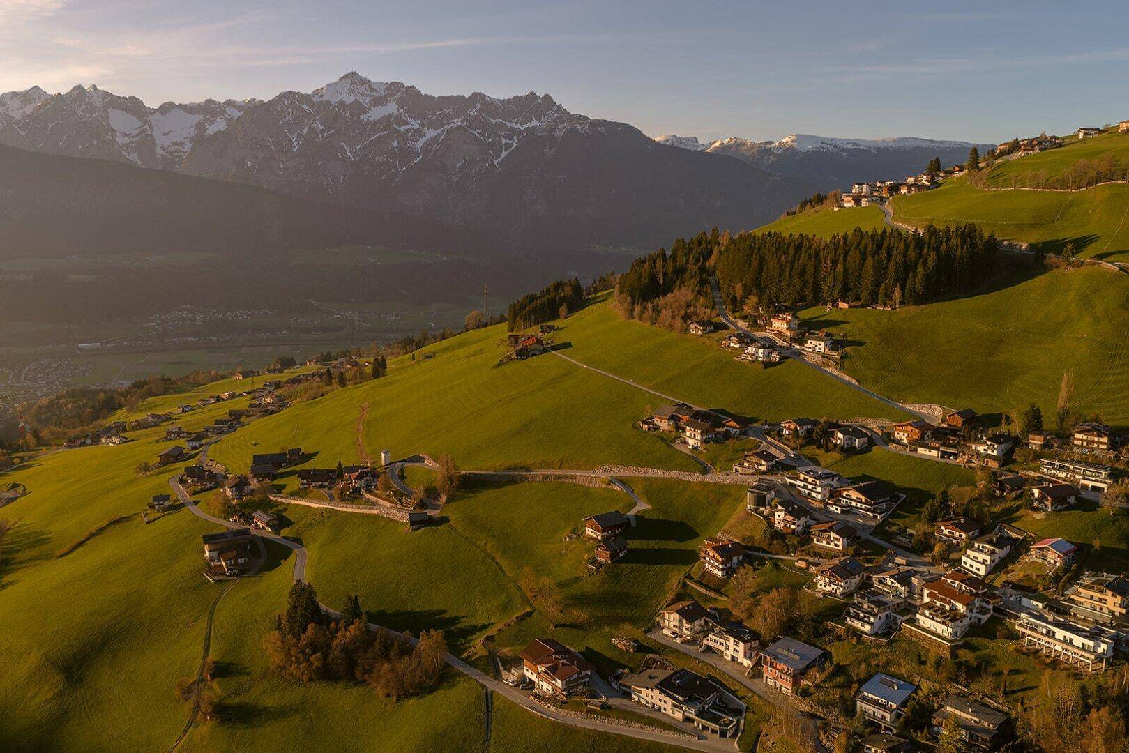 Panoramablick auf die Wohnsiedlung, harmonisch eingebettet in die grüne Natur mit den Alpen im Hintergrund.