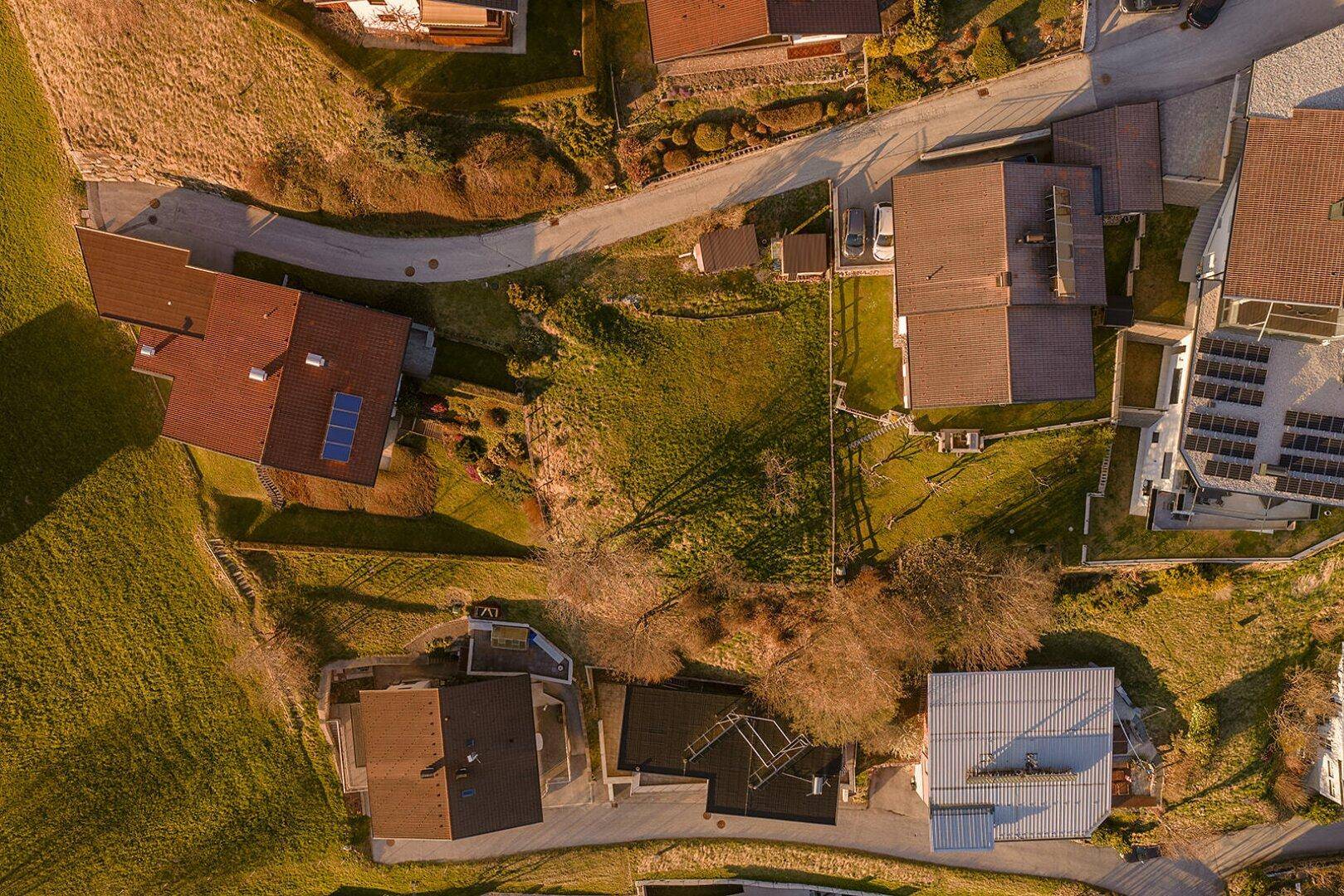 Detailreiche Luftansicht von Grundstücken und Häusern auf einem sonnigen Hang mit umliegender Natur.