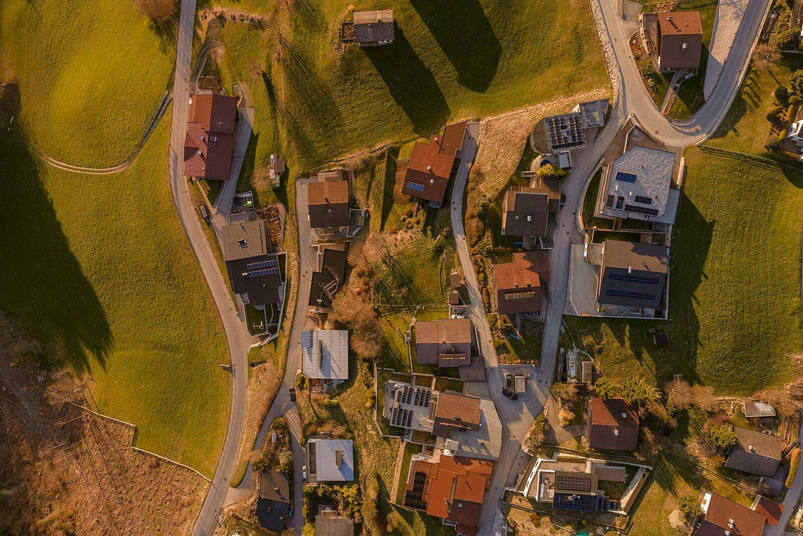 Luftaufnahme einer Wohnsiedlung auf einem grünen Hang mit mehreren Häusern und Wegen.