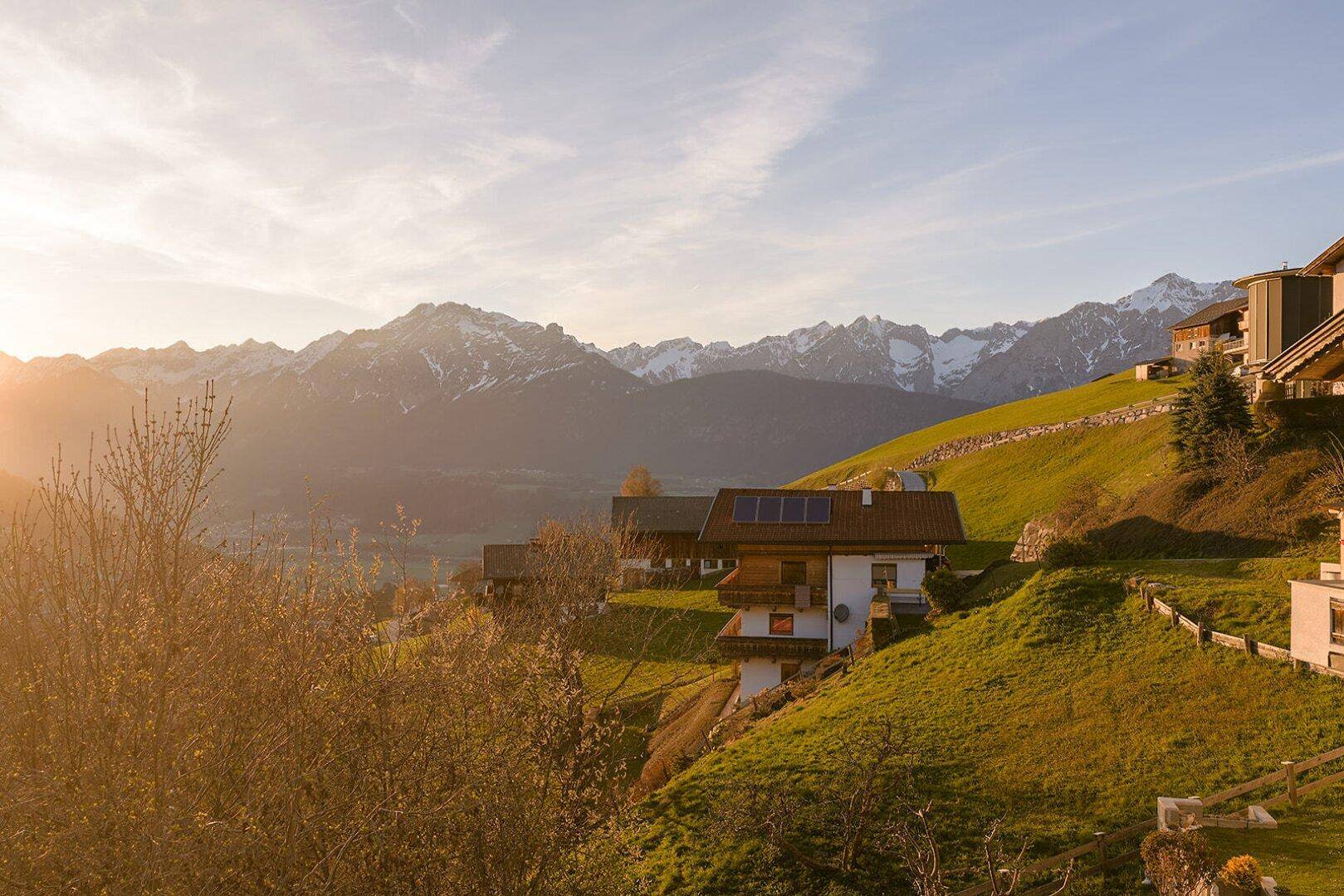 Ein Haus auf einem sonnigen Hang mit Photovoltaikanlage und einem weiten Blick auf die Bergwelt.