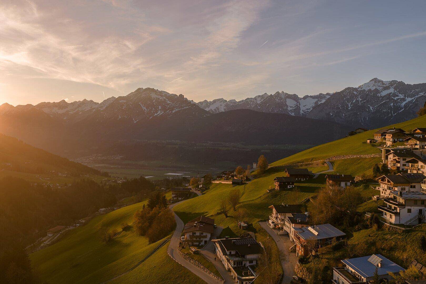 Malerischer Ausblick auf ein Tal mit verstreuten Häusern und majestätischen Bergen im warmen Abendlicht.
