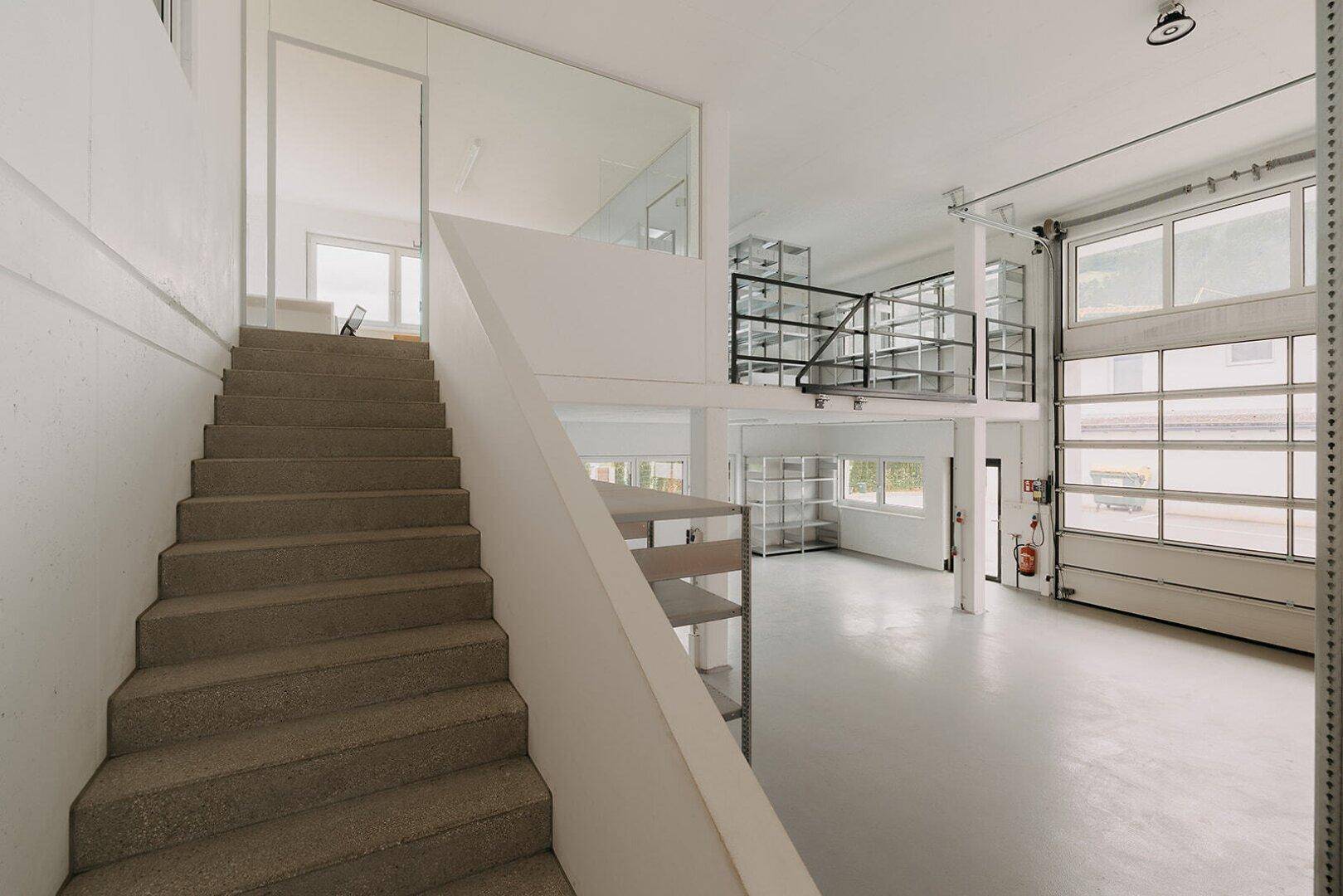 Treppenaufgang zu einem Zwischengeschoss in einer modernen Lagerhalle mit Betonboden und Rolltor.