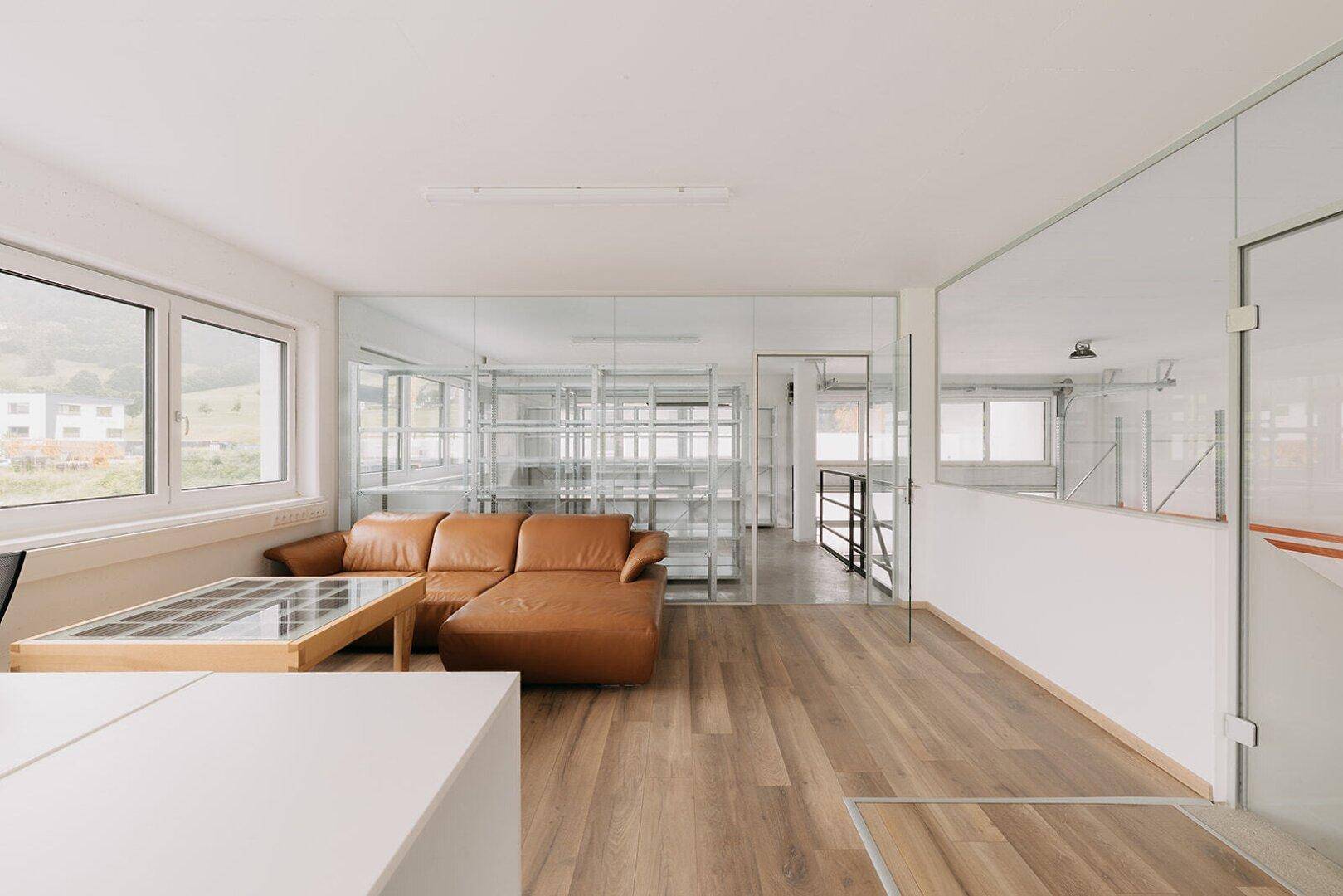 Offenes Büro mit Holzboden, Ledersofa und großen Fenstern mit Blick auf die Umgebung.