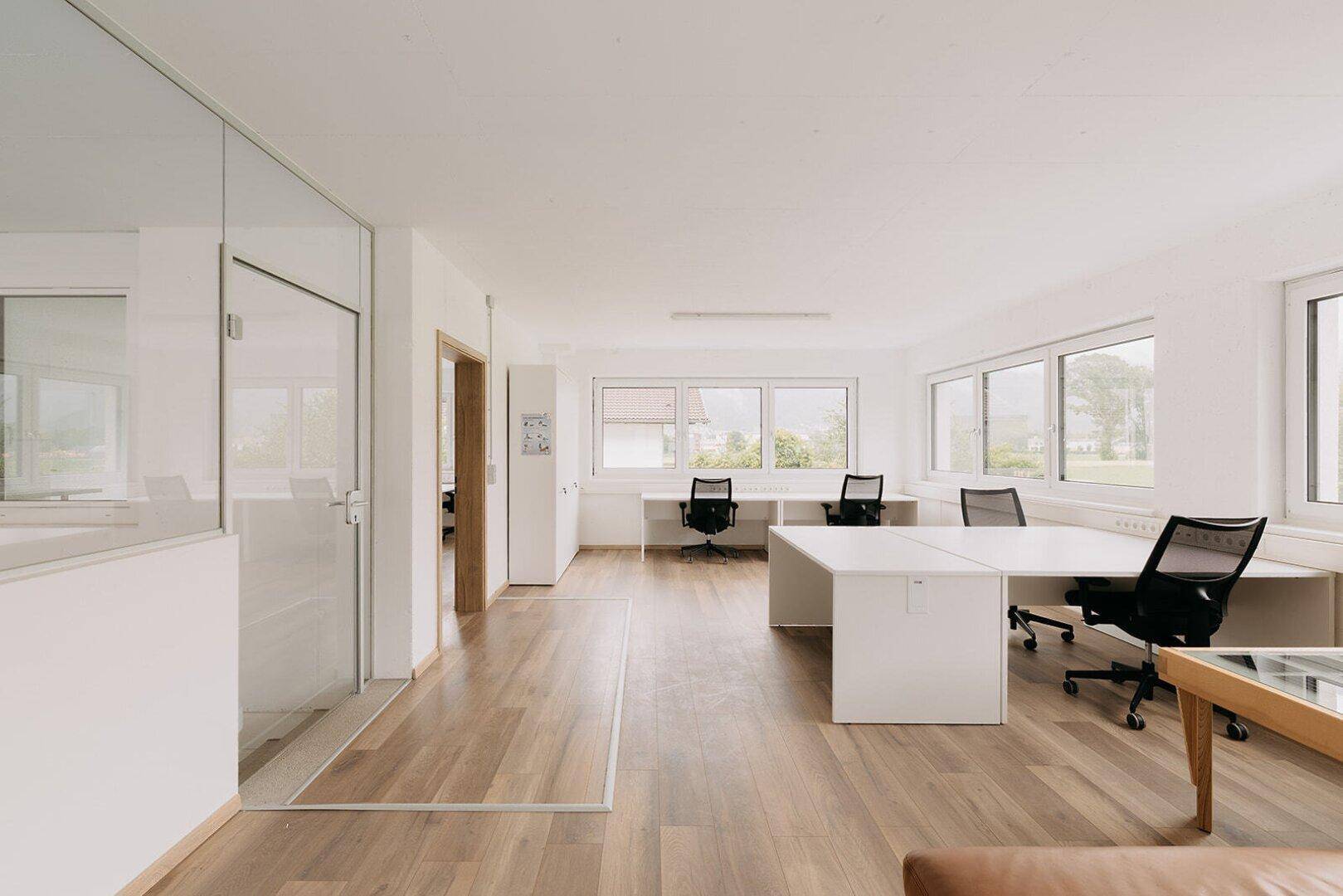 Helles Büro mit Holzboden, modernen Arbeitsplätzen und großen Fenstern für viel Tageslicht.