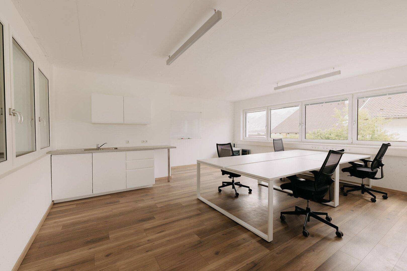 Modernes Büro mit Holzboden, Arbeitsplätzen und einer kleinen Küchenzeile für Mitarbeiter.
