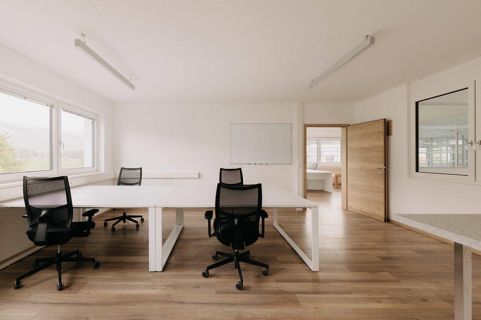 Geräumiger Bürobereich mit mehreren Arbeitsplätzen, großen Fenstern und hellem Holzboden.