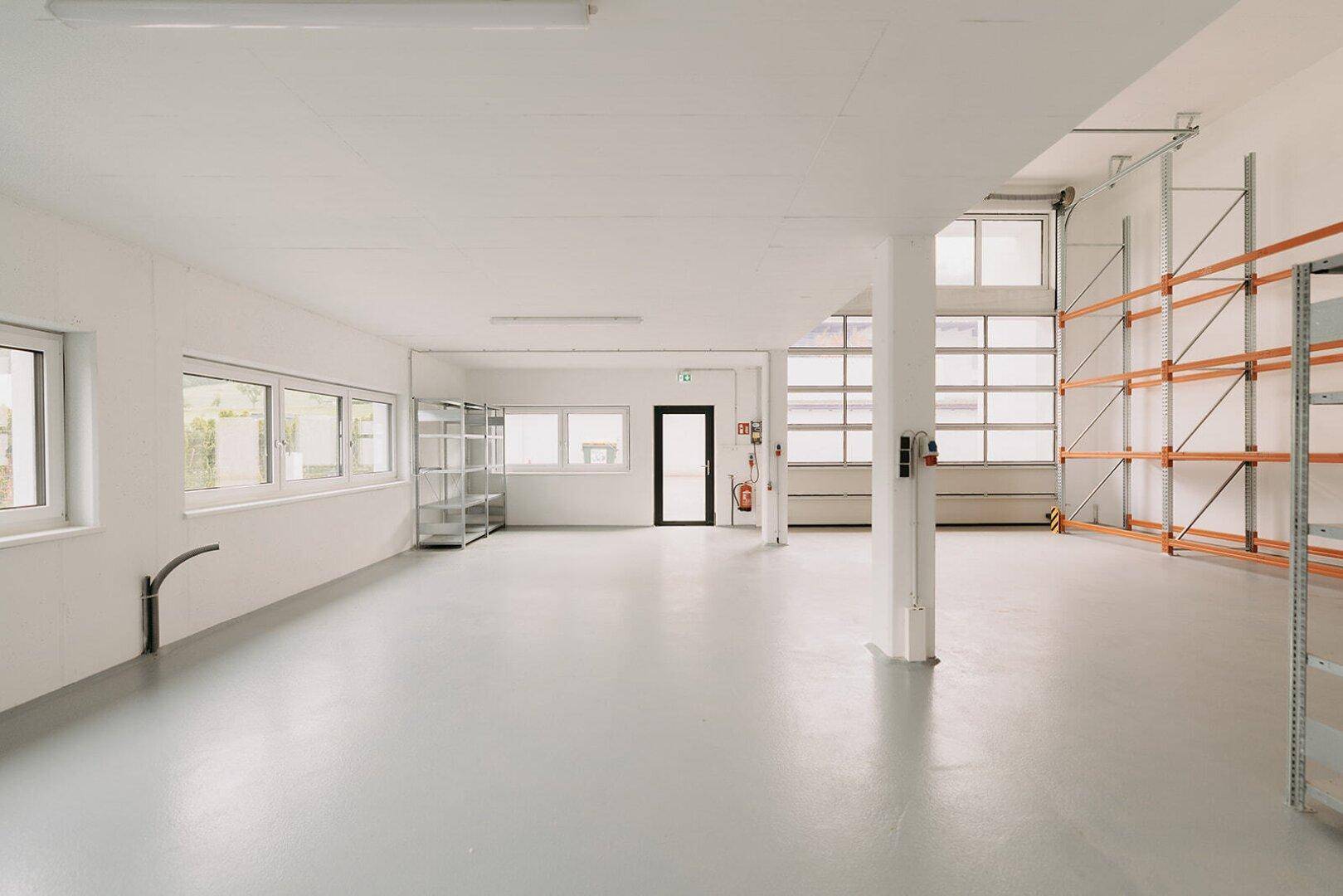Große, helle Lagerhalle mit Betonboden, vielen Fenstern und hohen Regalsystemen.