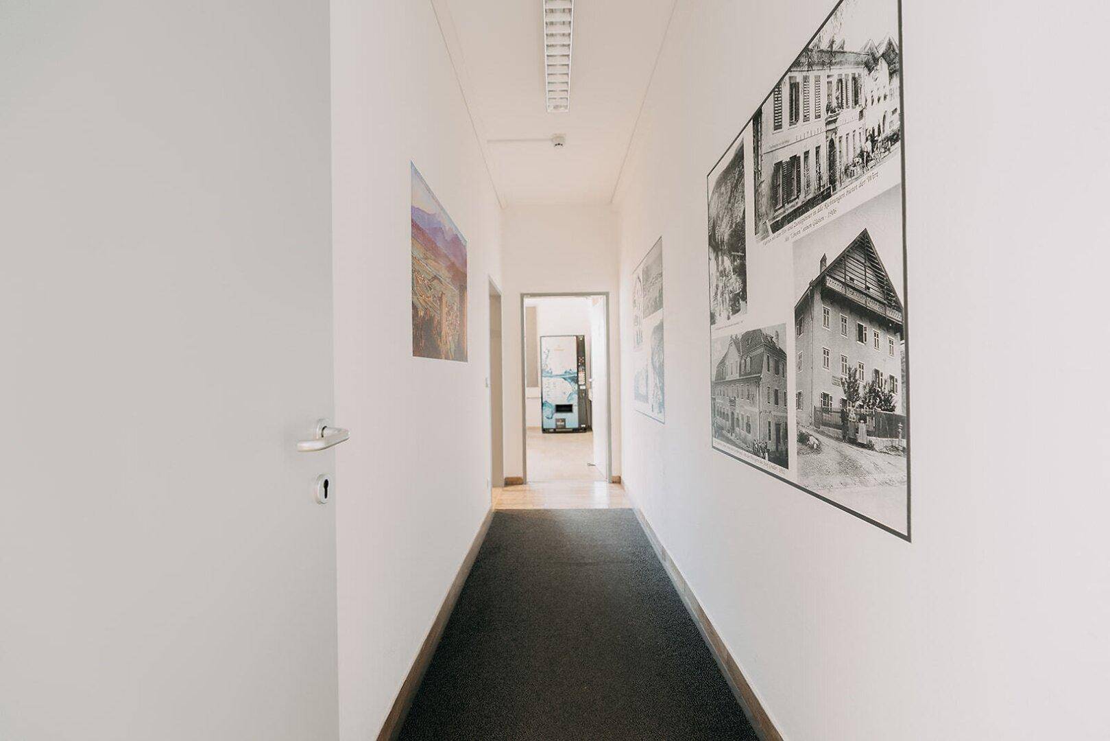 Heller Flur mit Kunst an den Wänden und einem Teppichläufer, der zu weiteren Räumen führt.