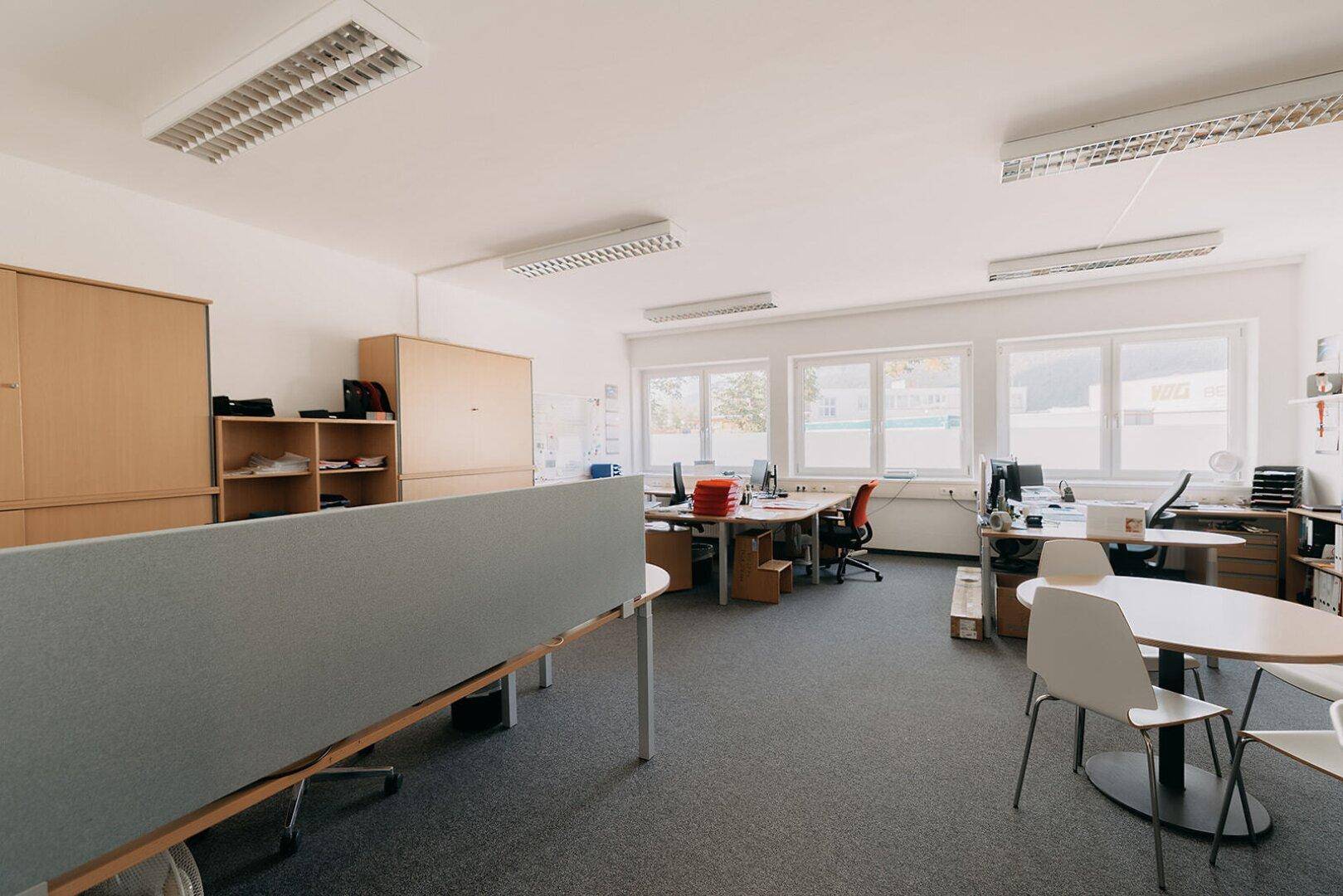 Geräumiges Büro mit Teppichboden, mehreren Schreibtischen und Trennwänden für Arbeitsbereiche.