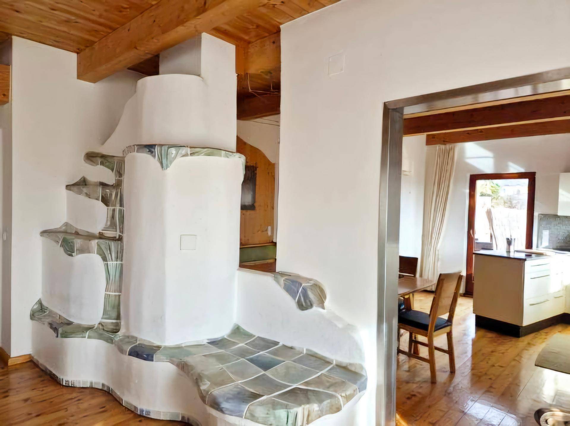 Ein kunstvoller Kachelofen mit integrierter Sitzbank und Holzbalkendecke, der den Wohnbereich prägt.