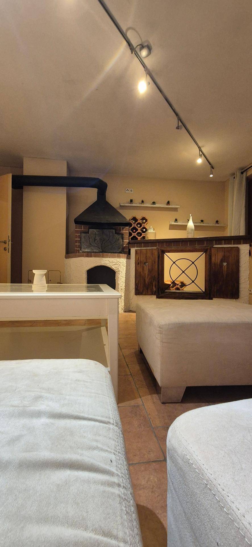 Rustikaler Wohnbereich mit großem Kaminofen, Fliesenboden und indirekter Beleuchtung.