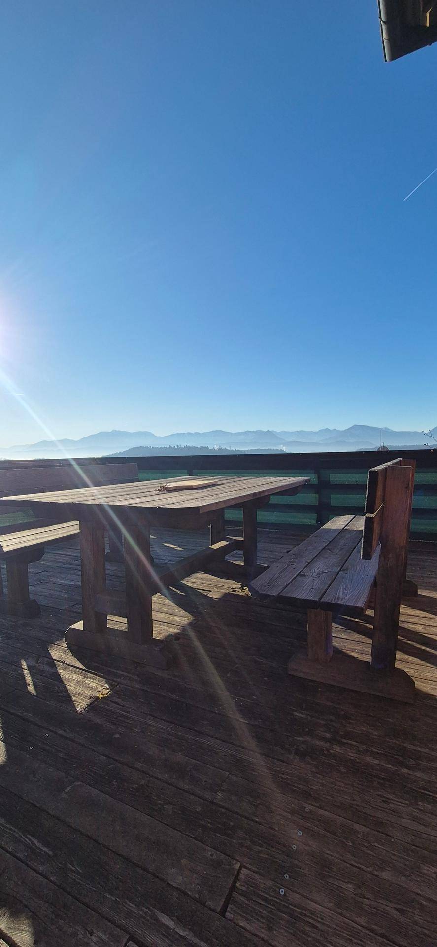 Sonnige Holzterrasse mit rustikalen Gartenmöbeln und weitem Bergblick.