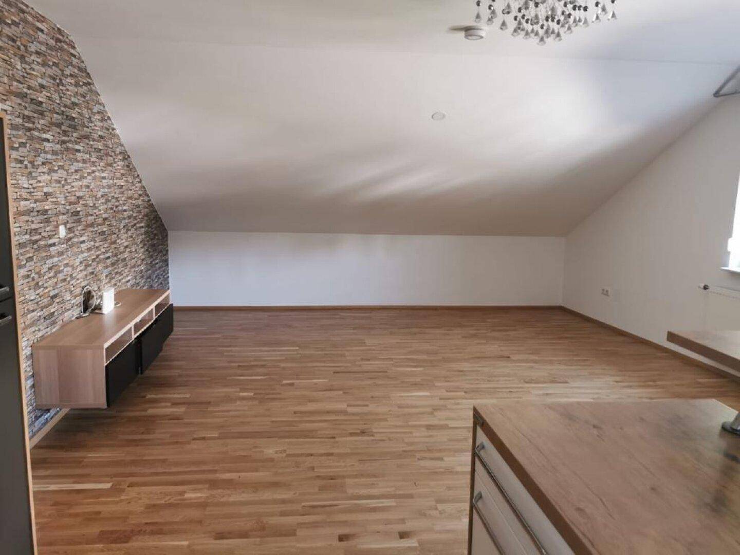 Großer Wohnbereich mit Holzboden, Dachschrägen und einer dekorativen Steinwand, unmöbliert.