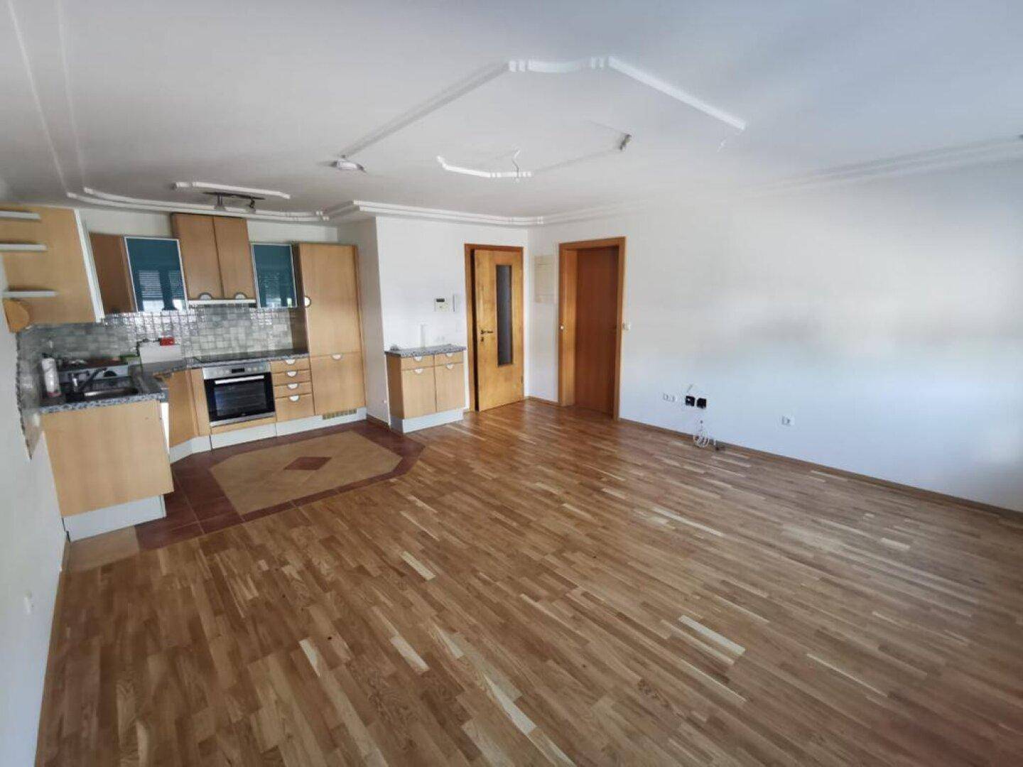 Offener Wohnbereich mit Holzboden, integrierter Küche und Deckenstuck, ideal für modernes Wohnen.