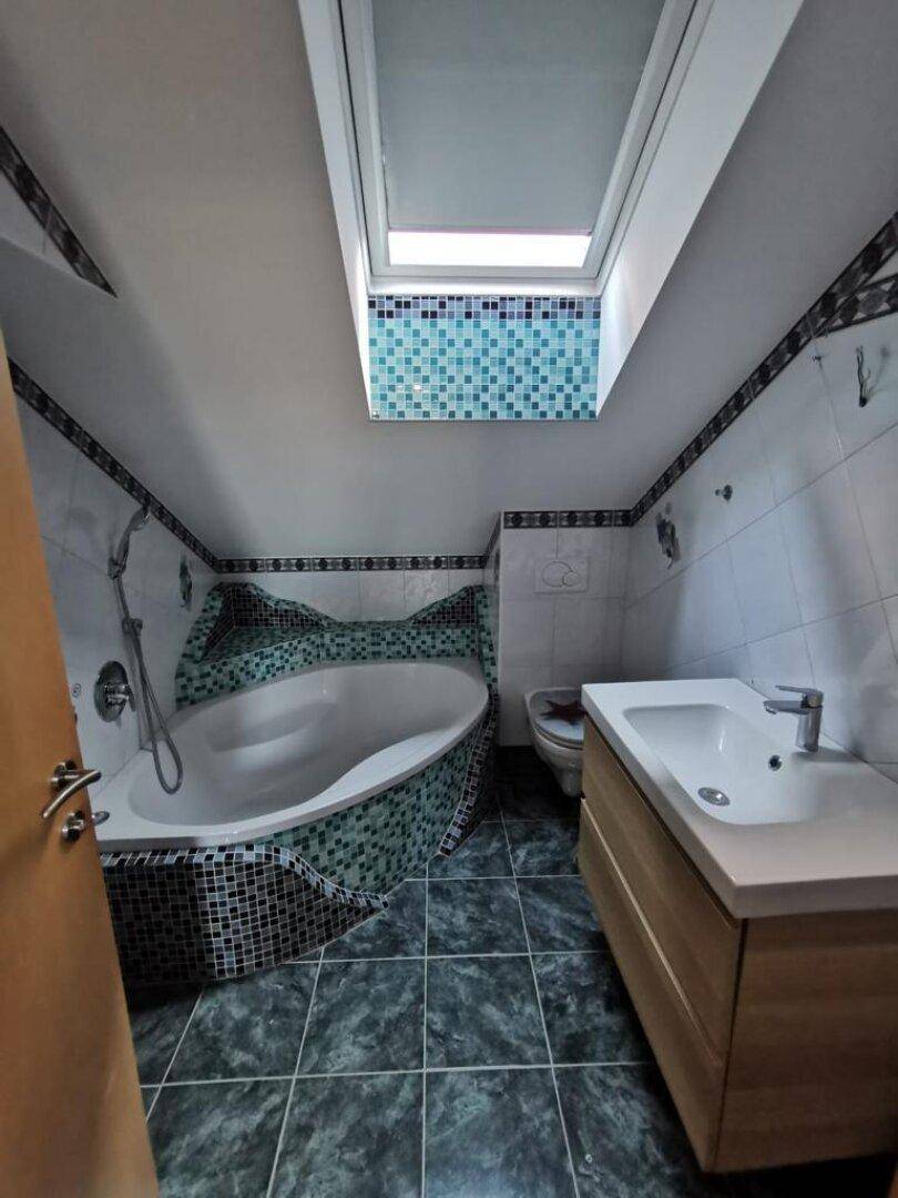 Badezimmer mit Eckbadewanne, Mosaikfliesen und Dachfenster, das viel Tageslicht hereinlässt.