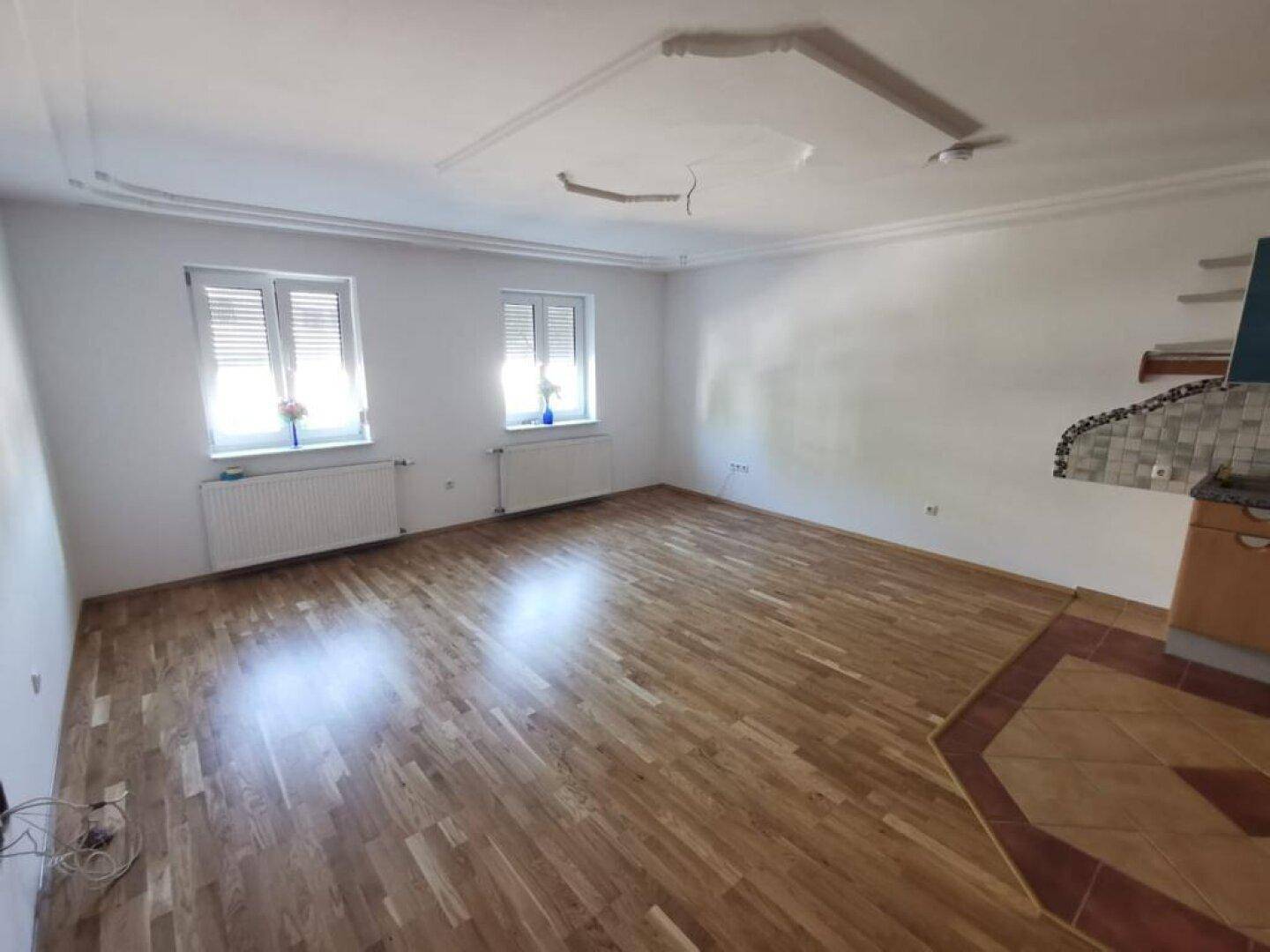 Geräumiger Wohnbereich mit Holzboden, zwei Fenstern und Deckenstuck, bereit zur individuellen Gestaltung.