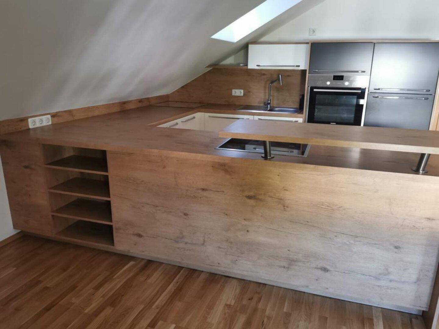 Moderne Küchenzeile mit Holzarbeitsplatten, integriertem Kochfeld und Dachfenster für Helligkeit.