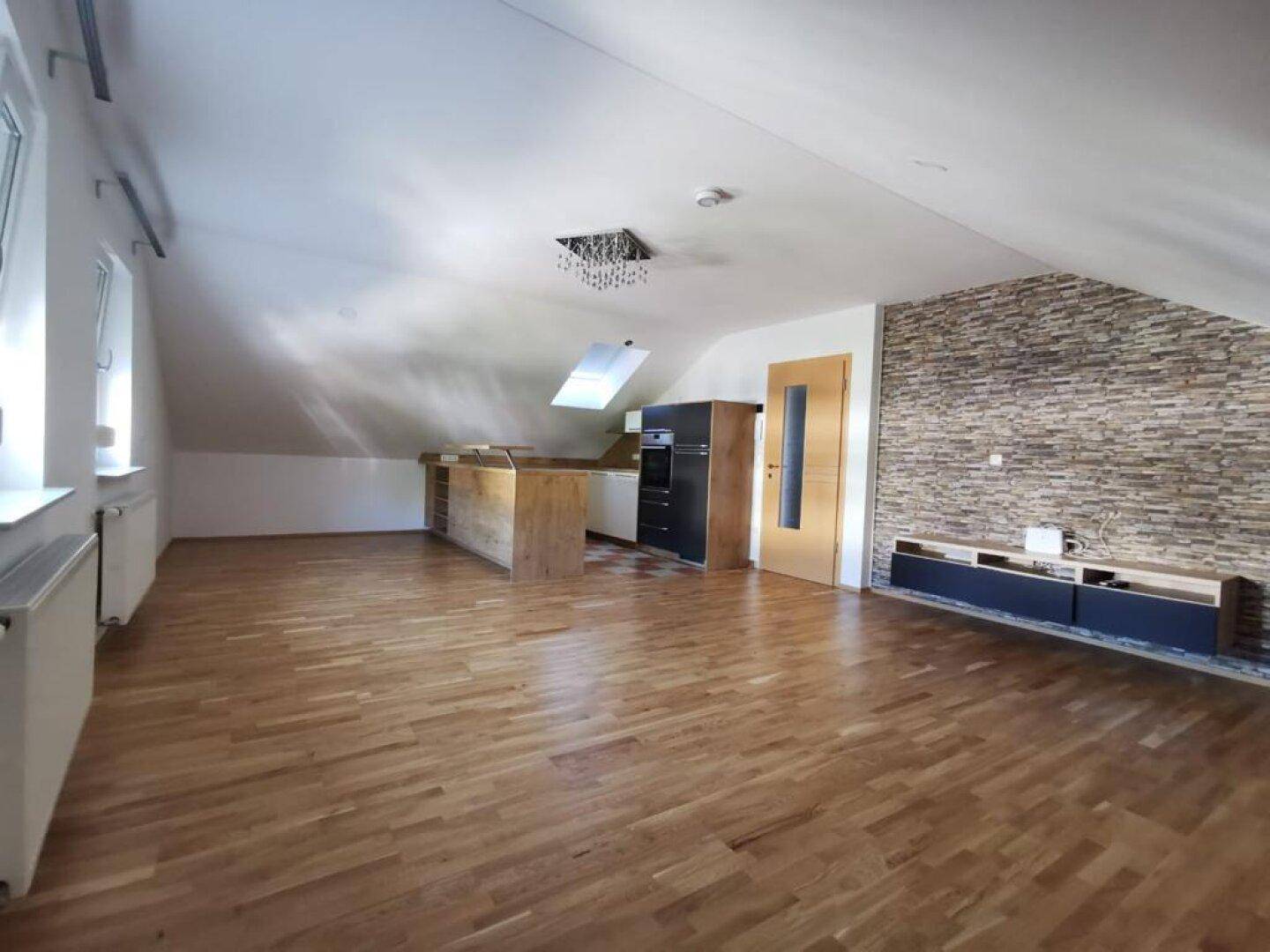 Offener Wohnbereich mit Holzboden, Küchenzeile und dekorativer Steinwand, unter Dachschrägen gelegen.
