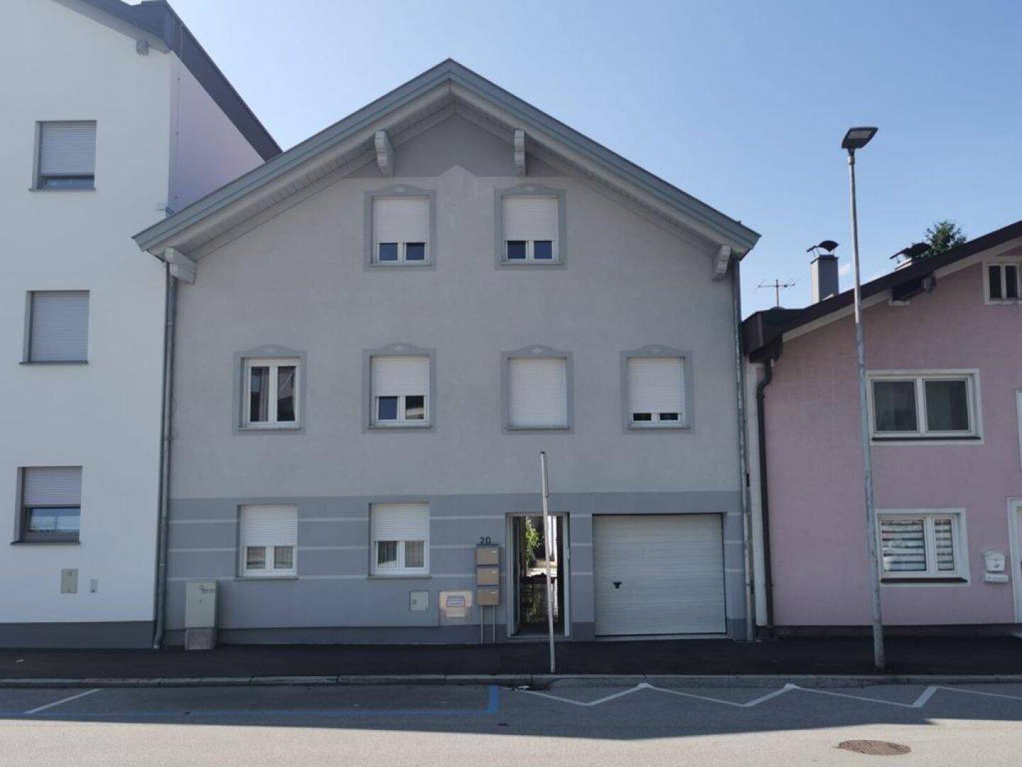 Graues Mehrfamilienhaus mit mehreren Fenstern und einer integrierten Garage im Erdgeschoss.