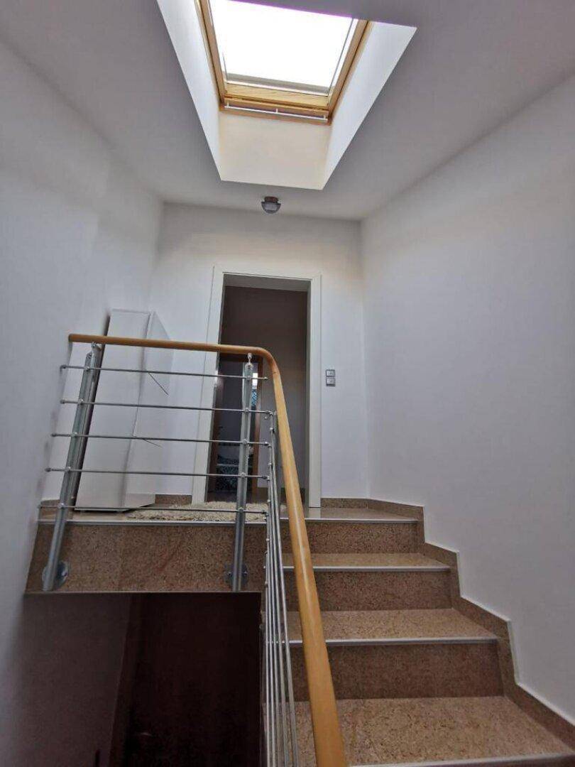 Heller Treppenaufgang mit Granitstufen, Edelstahlgeländer und einem Dachfenster für natürliches Licht.